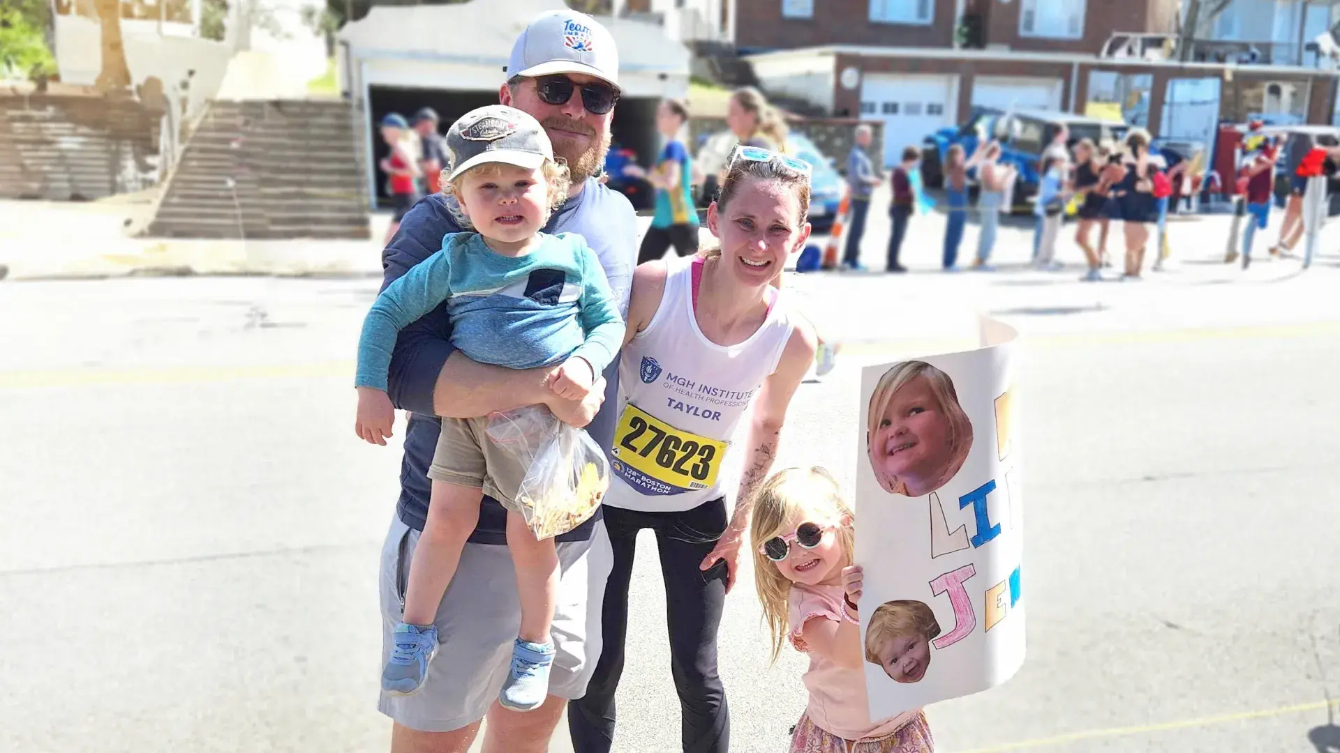 women in tank top with race bib attached smiles with man and two children in the street
