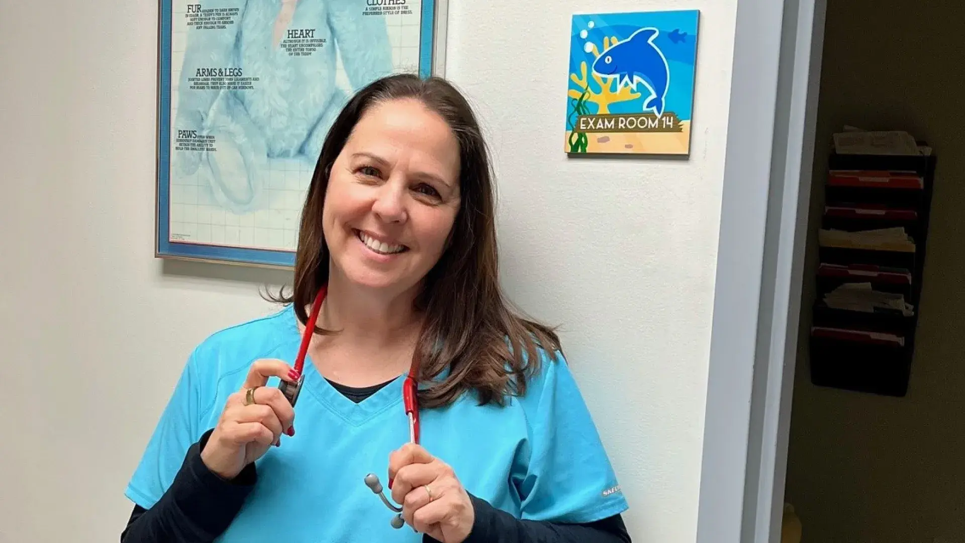 woman in blue scrubs with stethoscope around neck and big smile