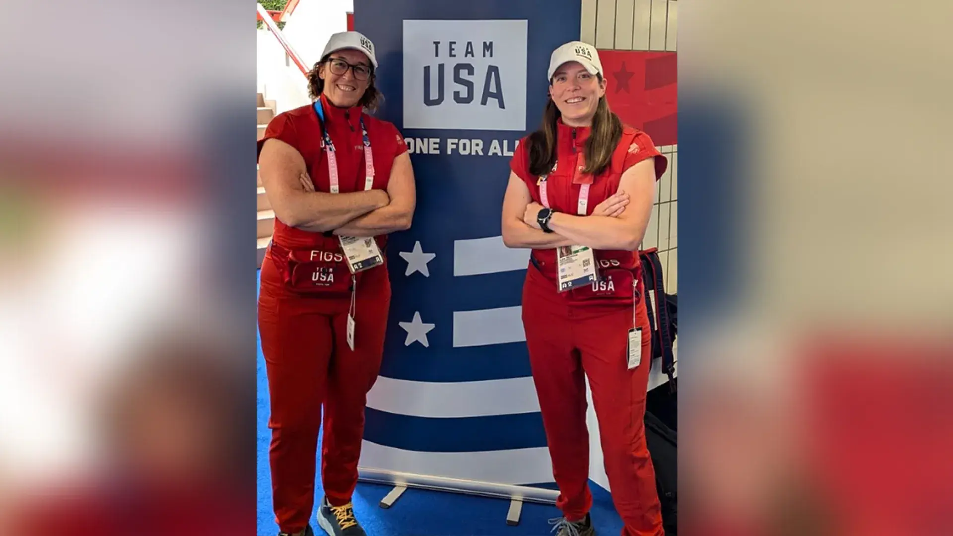 two women in red outfits pose in front of a team USA sign