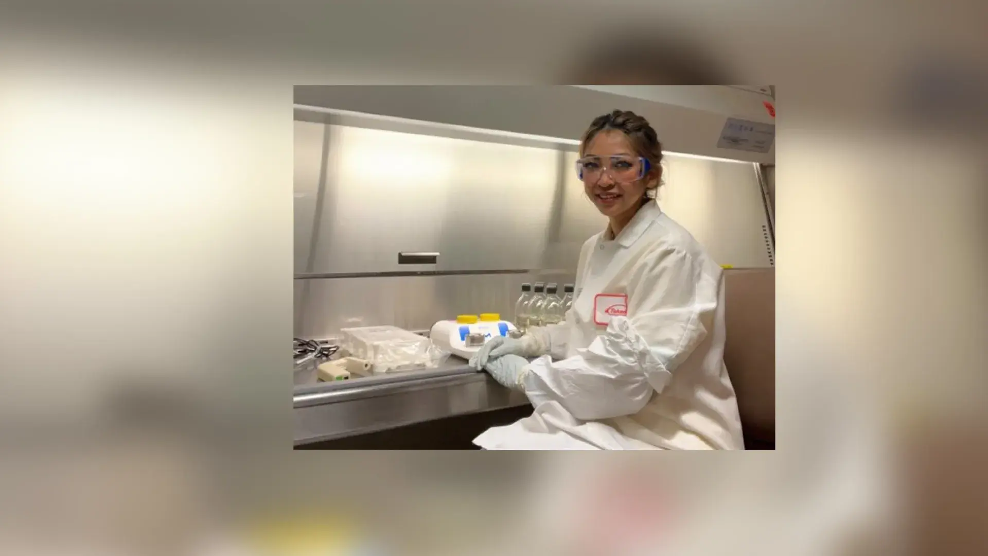junny sits in a lab with a lab coat and lab glasses on