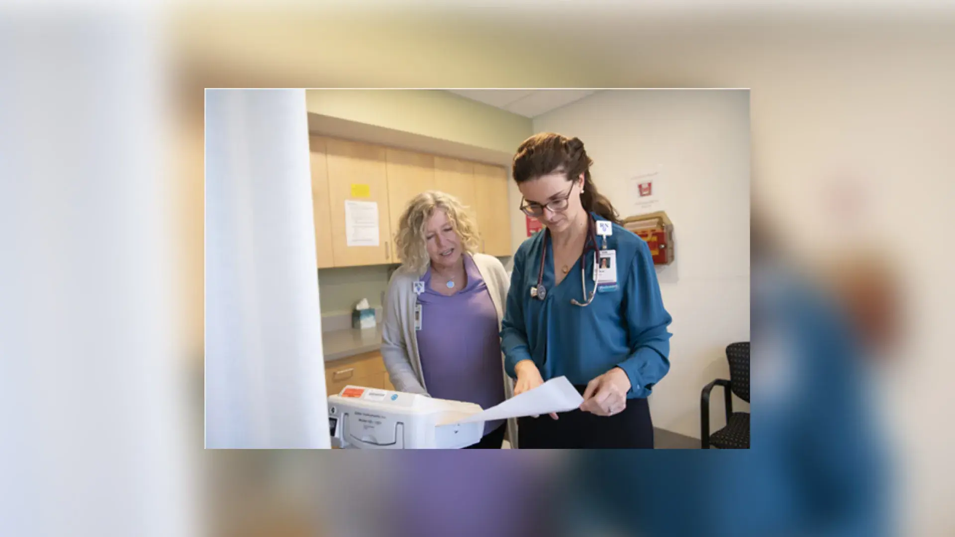 a woman with a stethoscope on looks at a paper while another woman looks over her shoulder