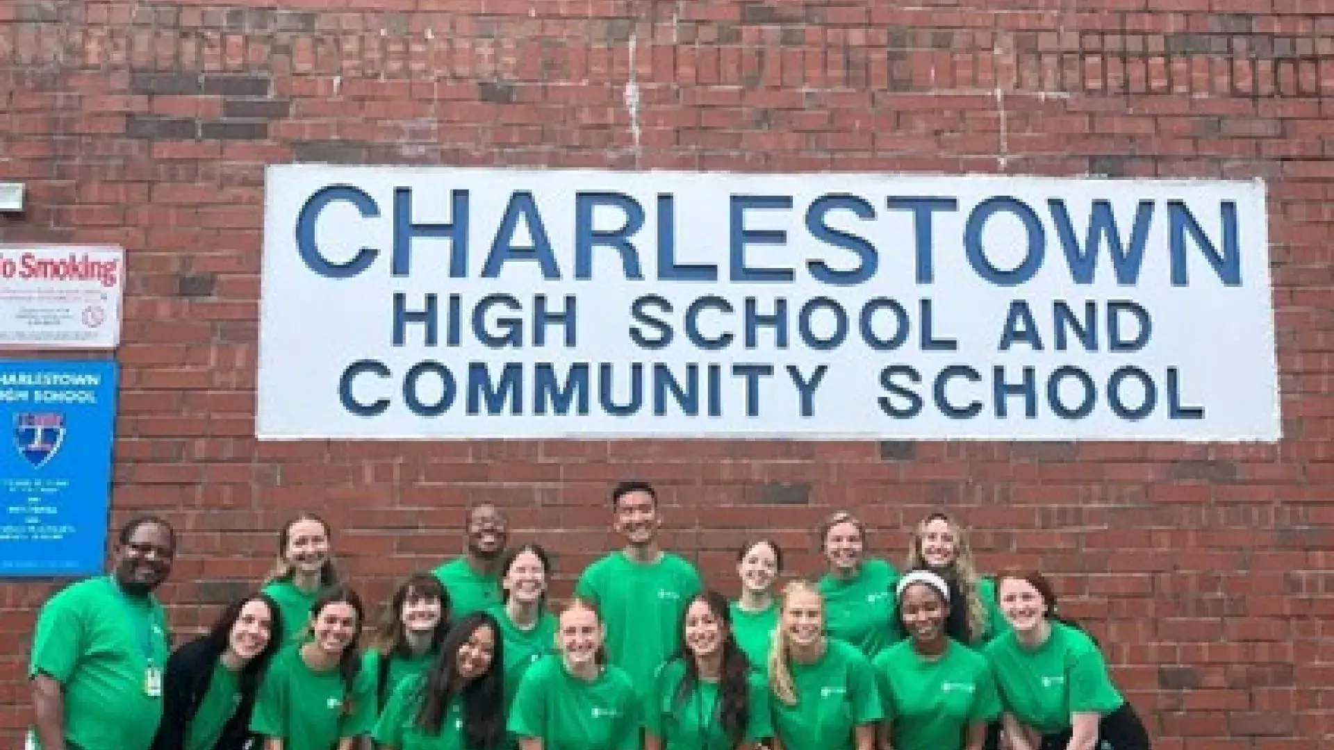 A group of people pose in front a sign that says, Charlestown High School and Community School 