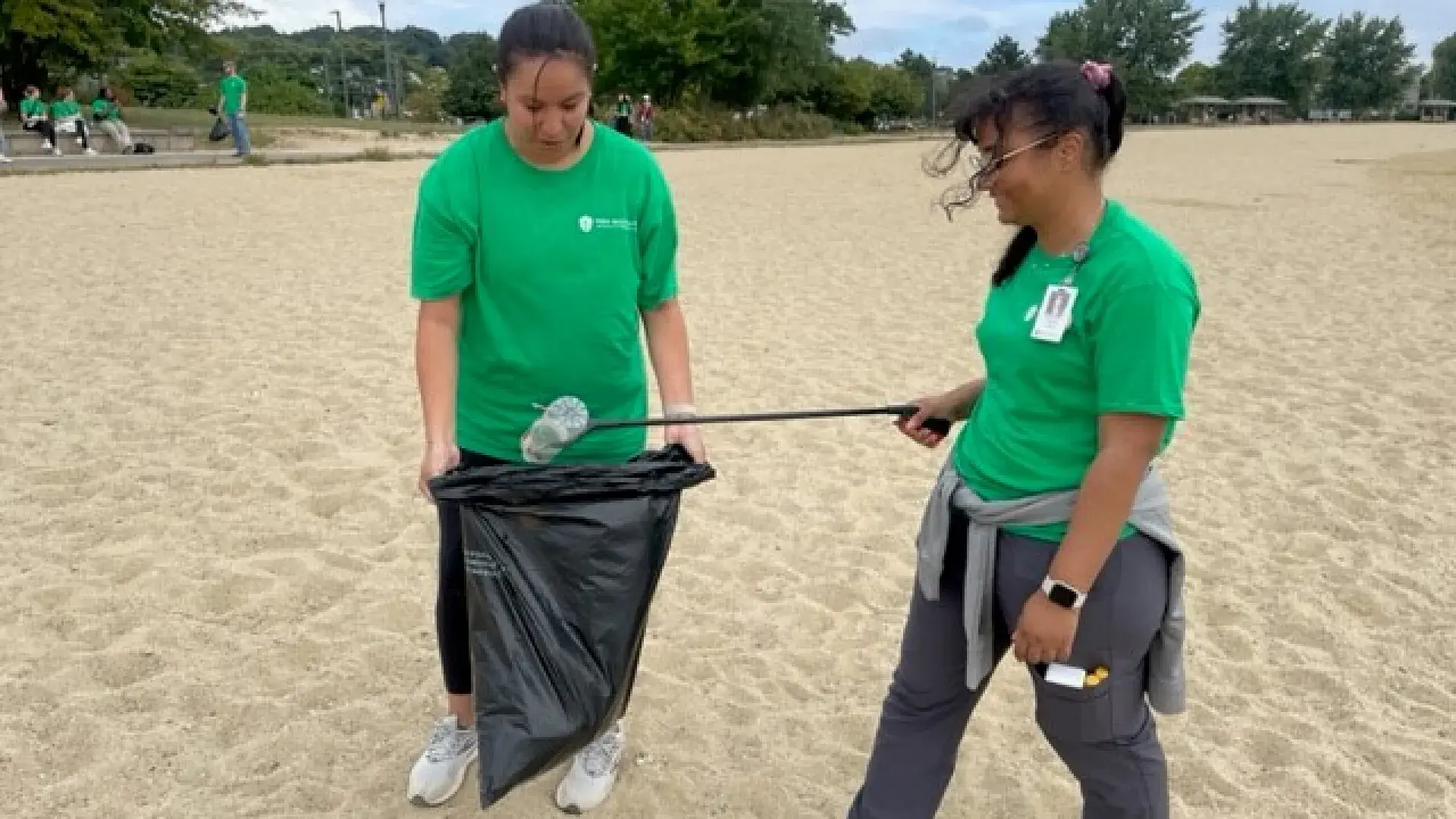 Two woman walk on a beach pick up trash