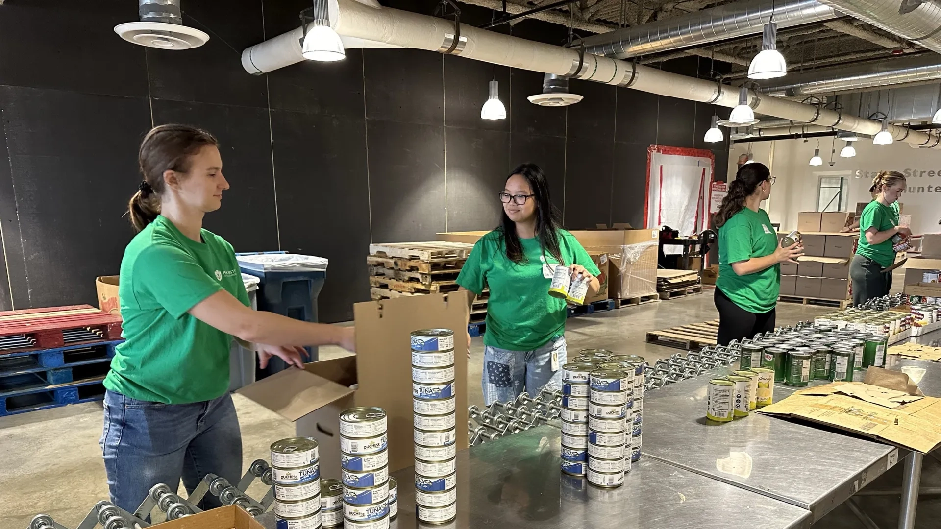 A woman passes a box on an assembly line to a waiting person while two other people are further down the line