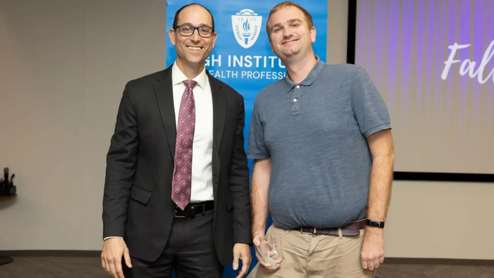 two men stand in front of MGH banner with award