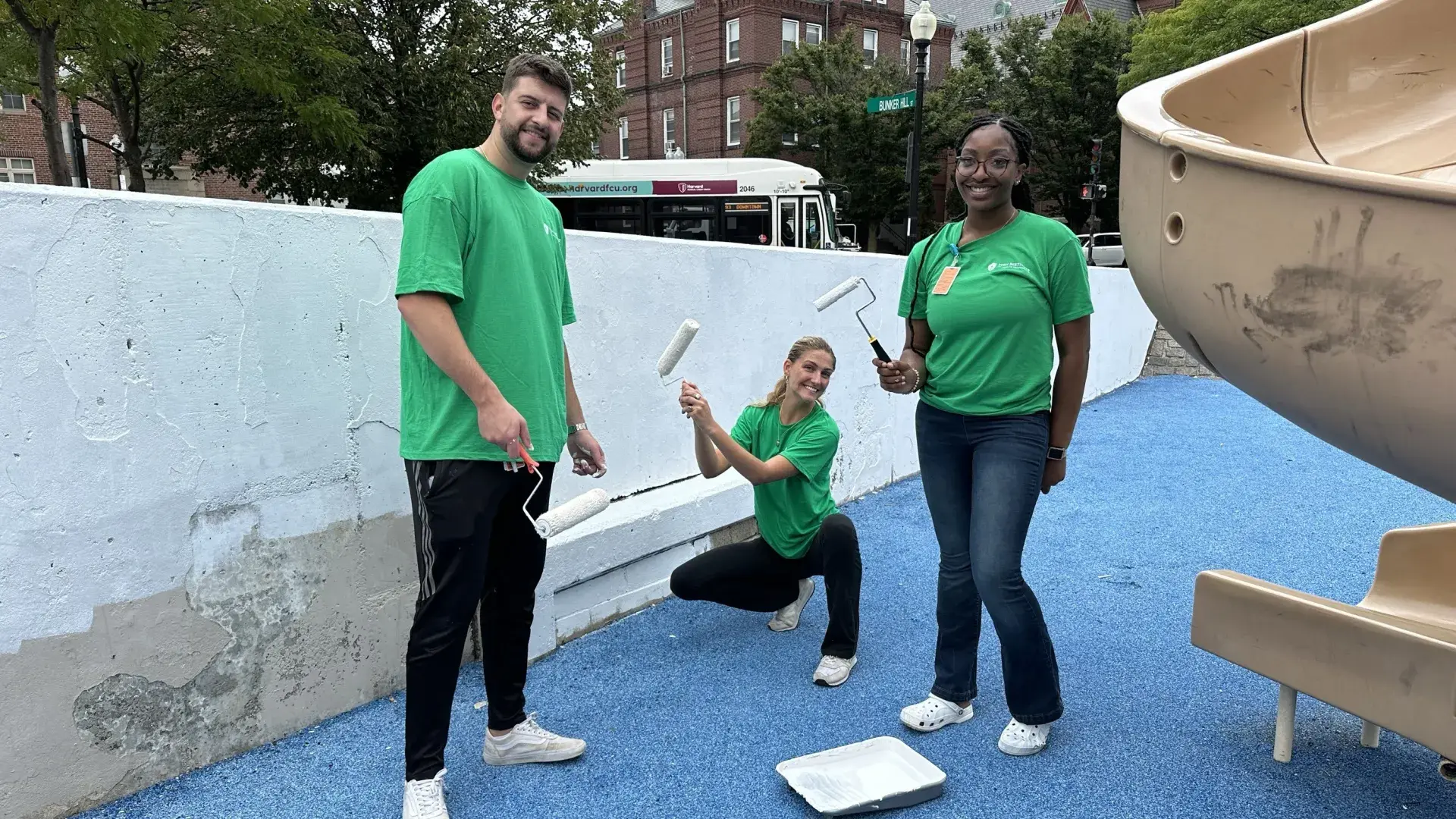 A man and two women pose in front of a wall being painted white while holding paint rollers