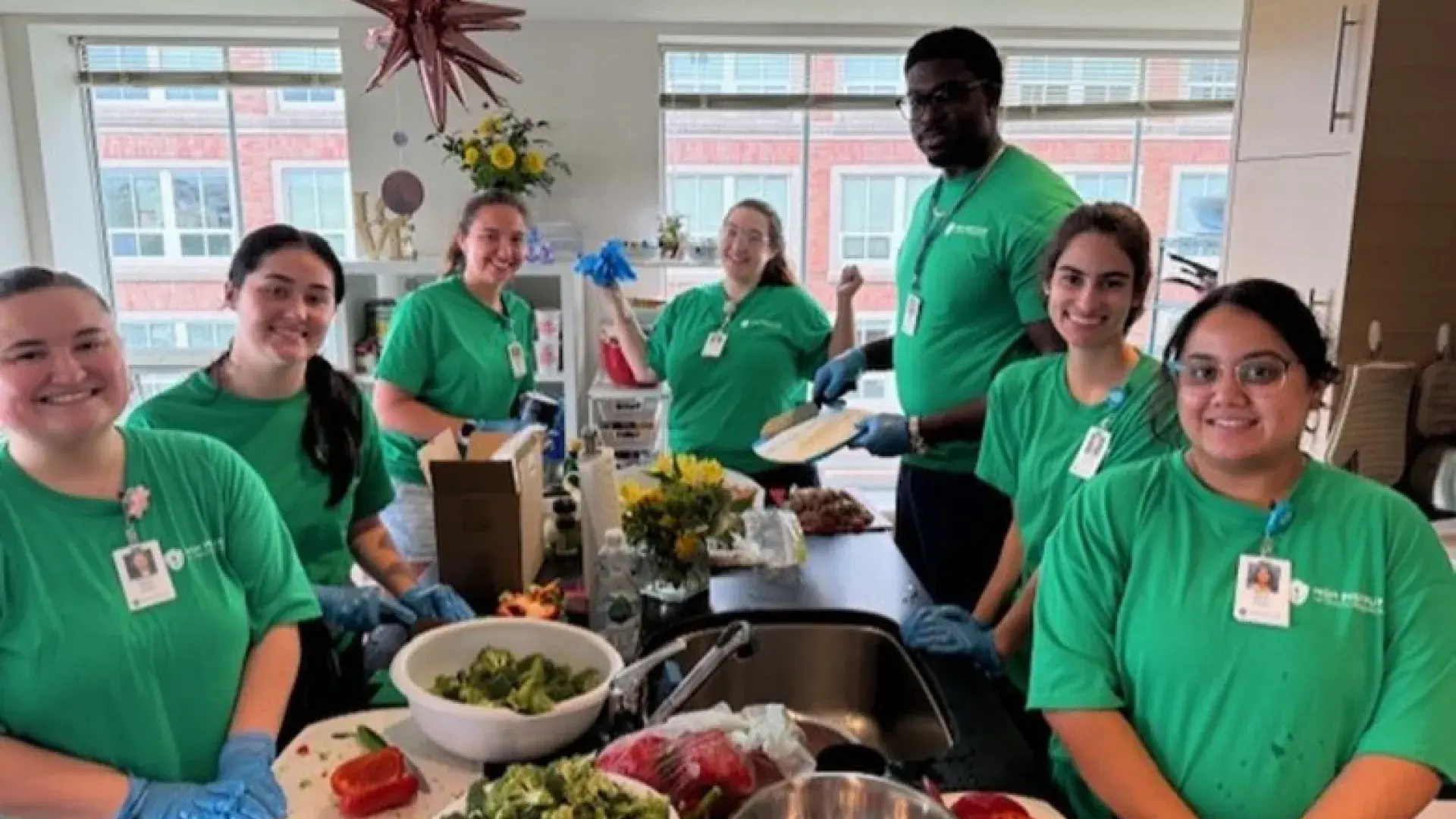 People pose around a kitchen workspace with vegetables in various states of being cut and prepared