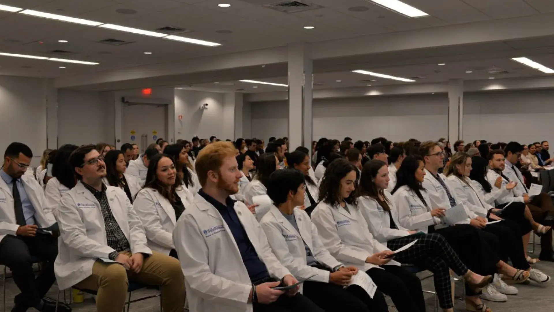 People wearing white physician coats sit in an audience