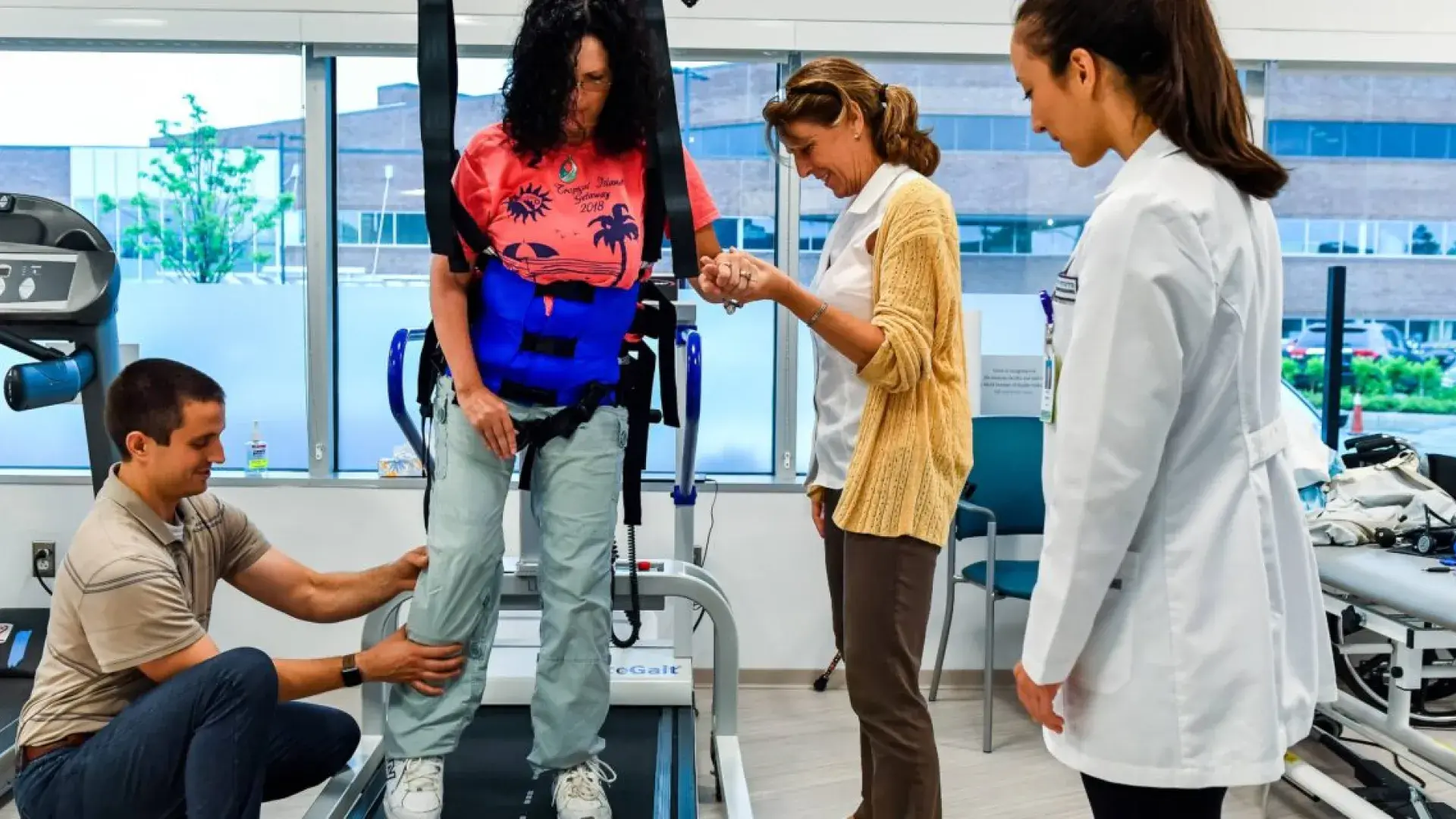 a woman in a harness walks on a treadmill surrounded by caregivers