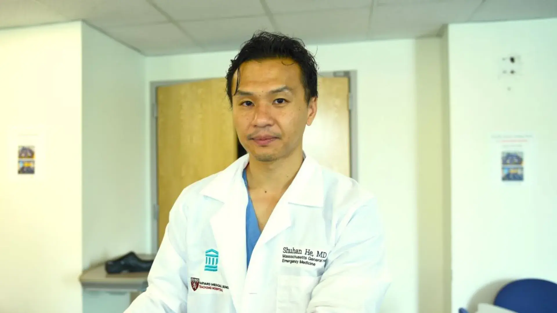 Doctor in lab coat looking into camera; coat has name and hosital affiliation 