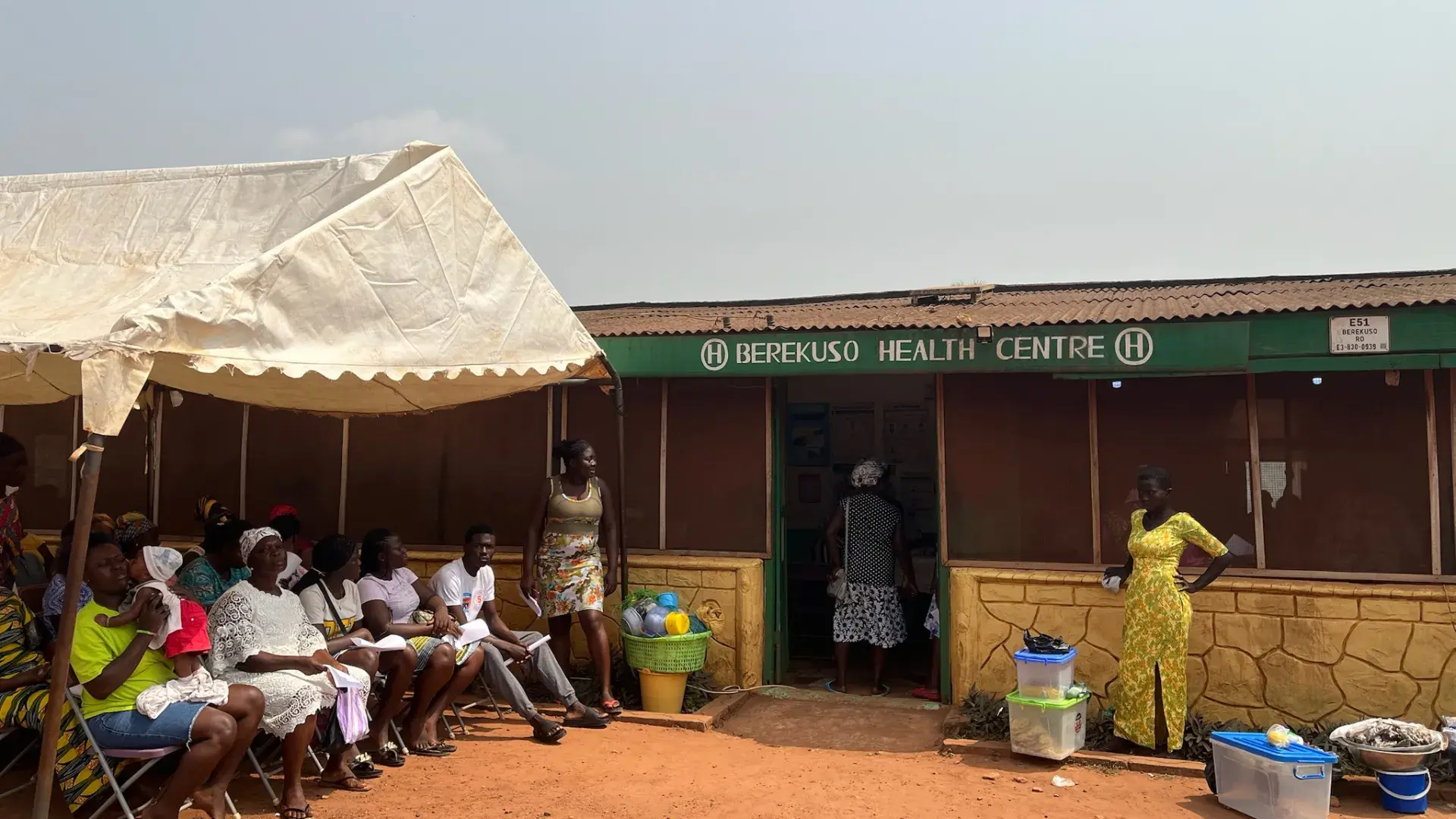 A tent with people sitting under it next to a health center