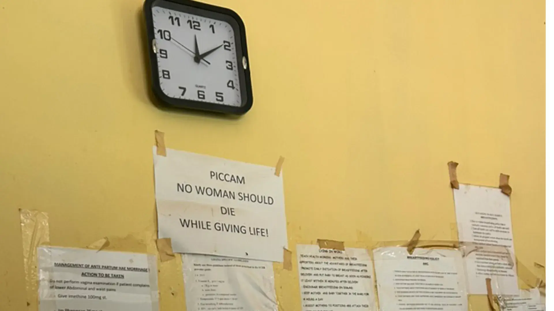 A sign saying "No woman should die giving life" taped to the wall