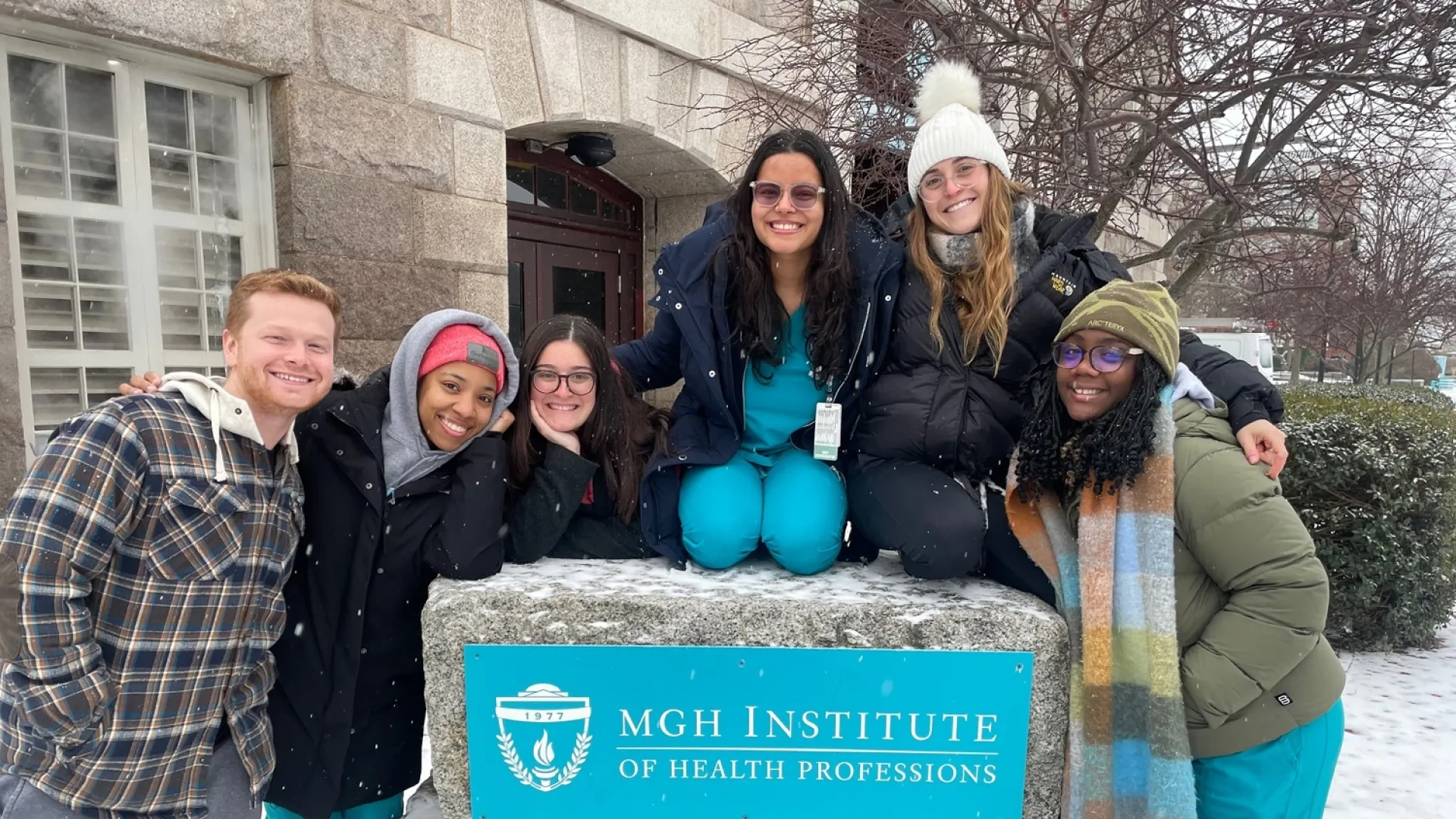 students in scrubs gather around the University sign on campus