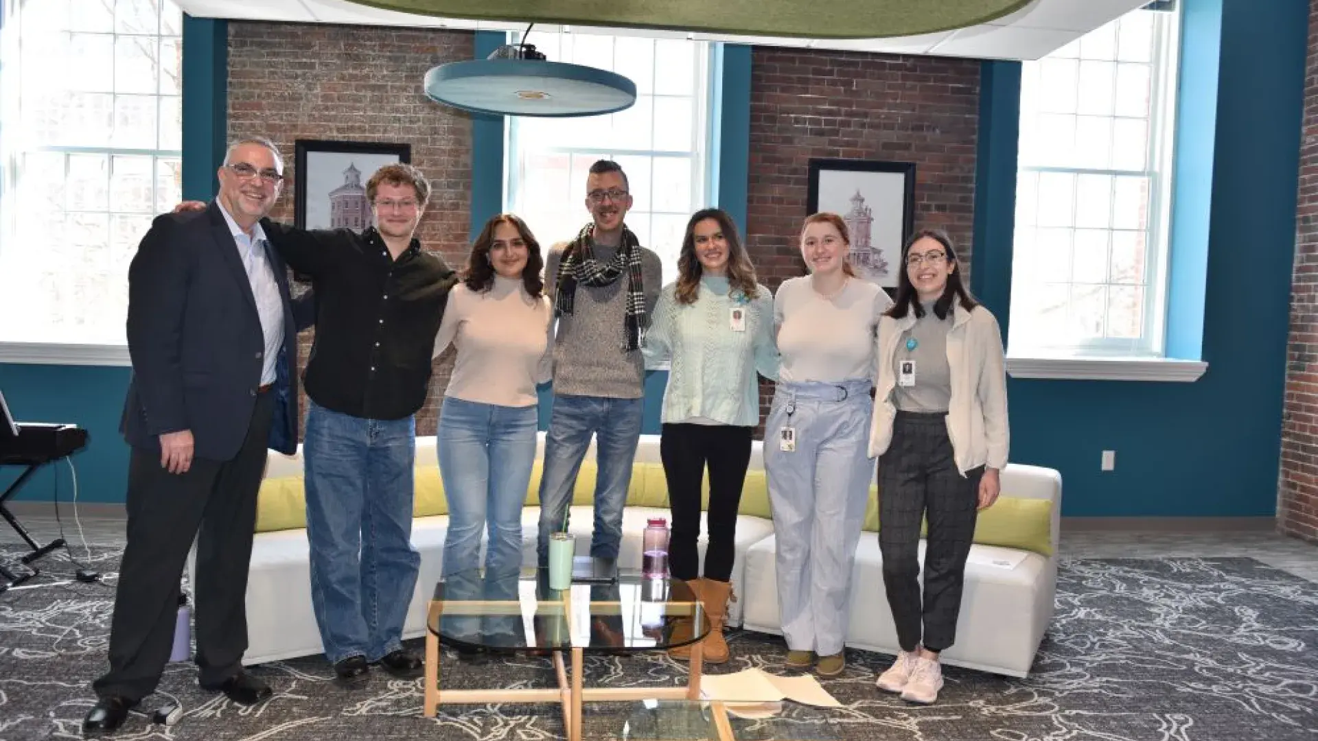 Seven people pose together in front of a couch