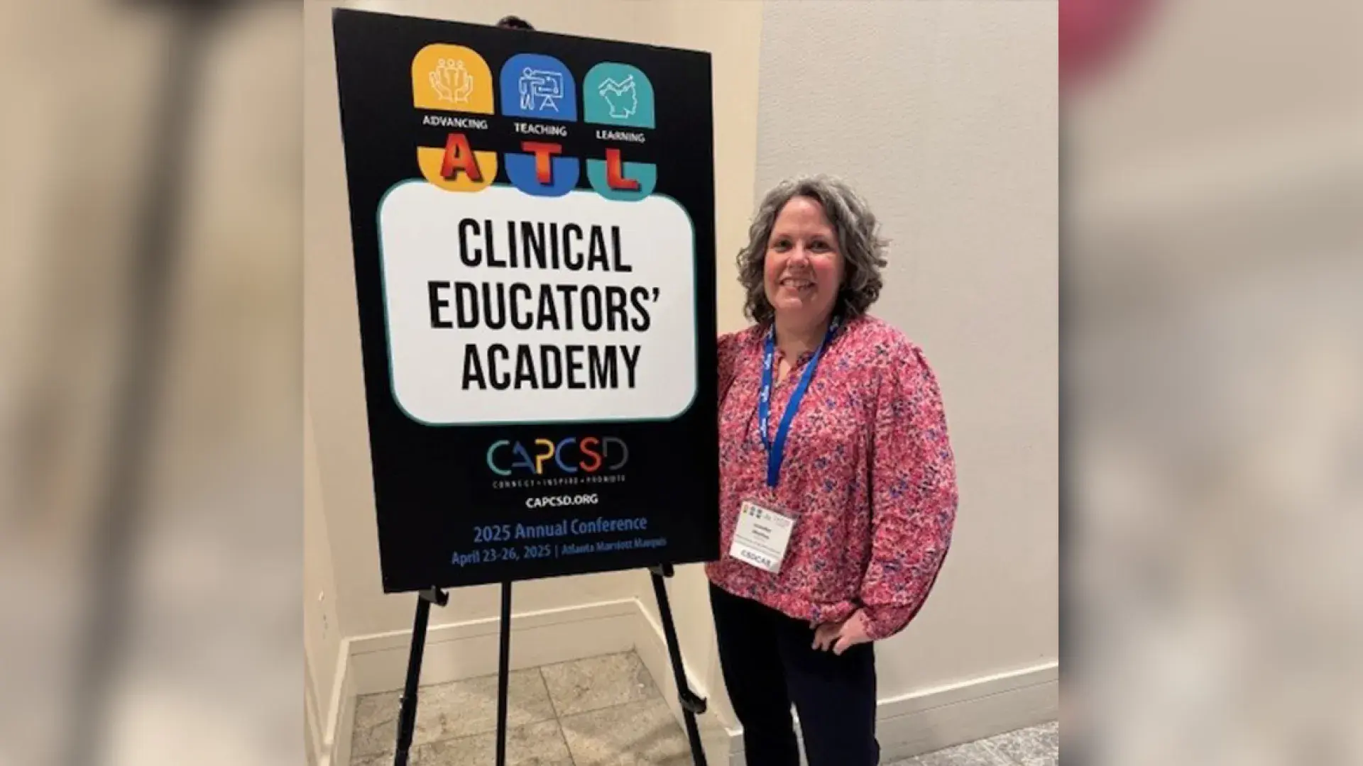 A woman stands in front of a sign that says Clinical Educators' Academy