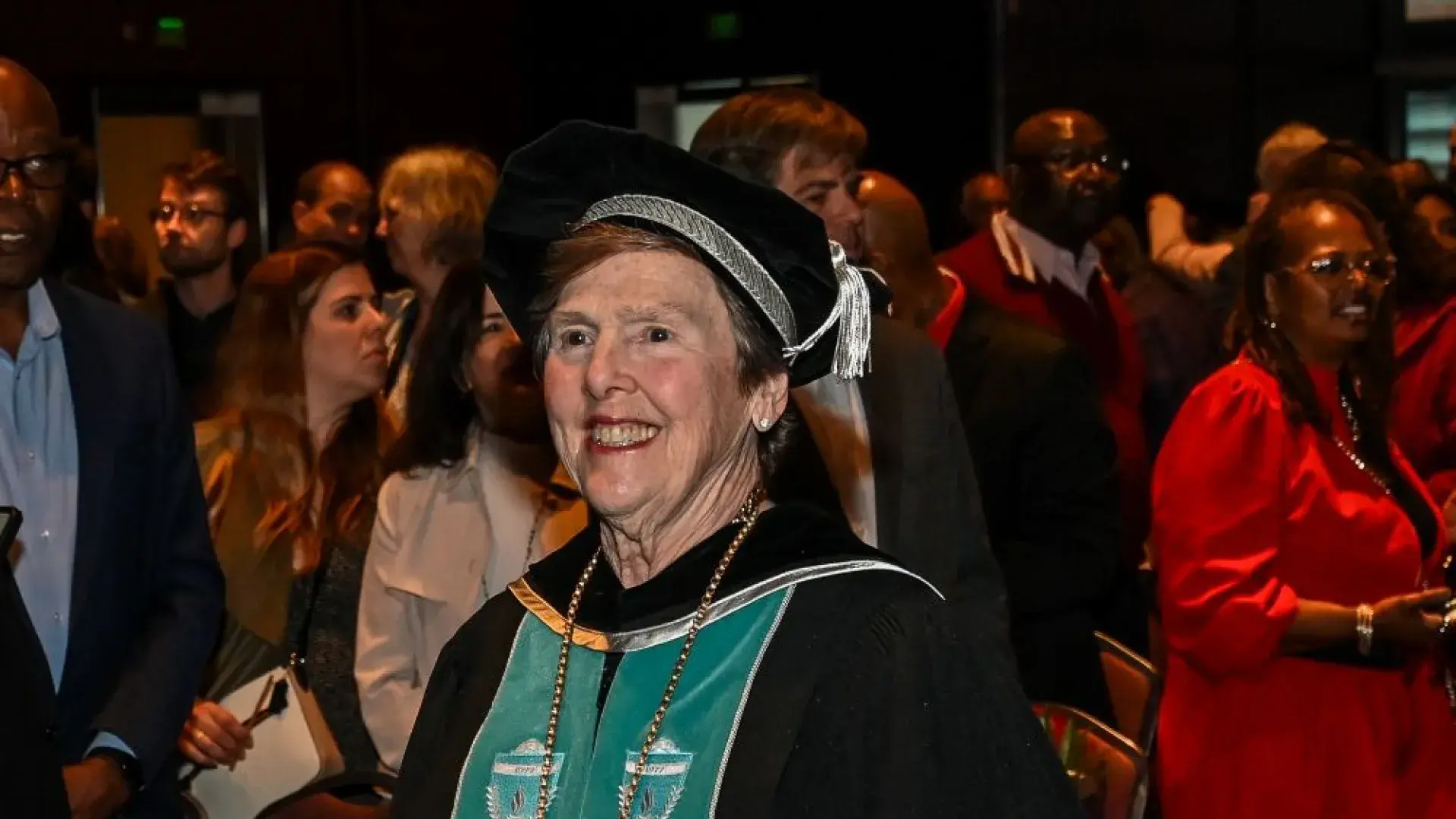 A woman in a commencement robe walks through an audience