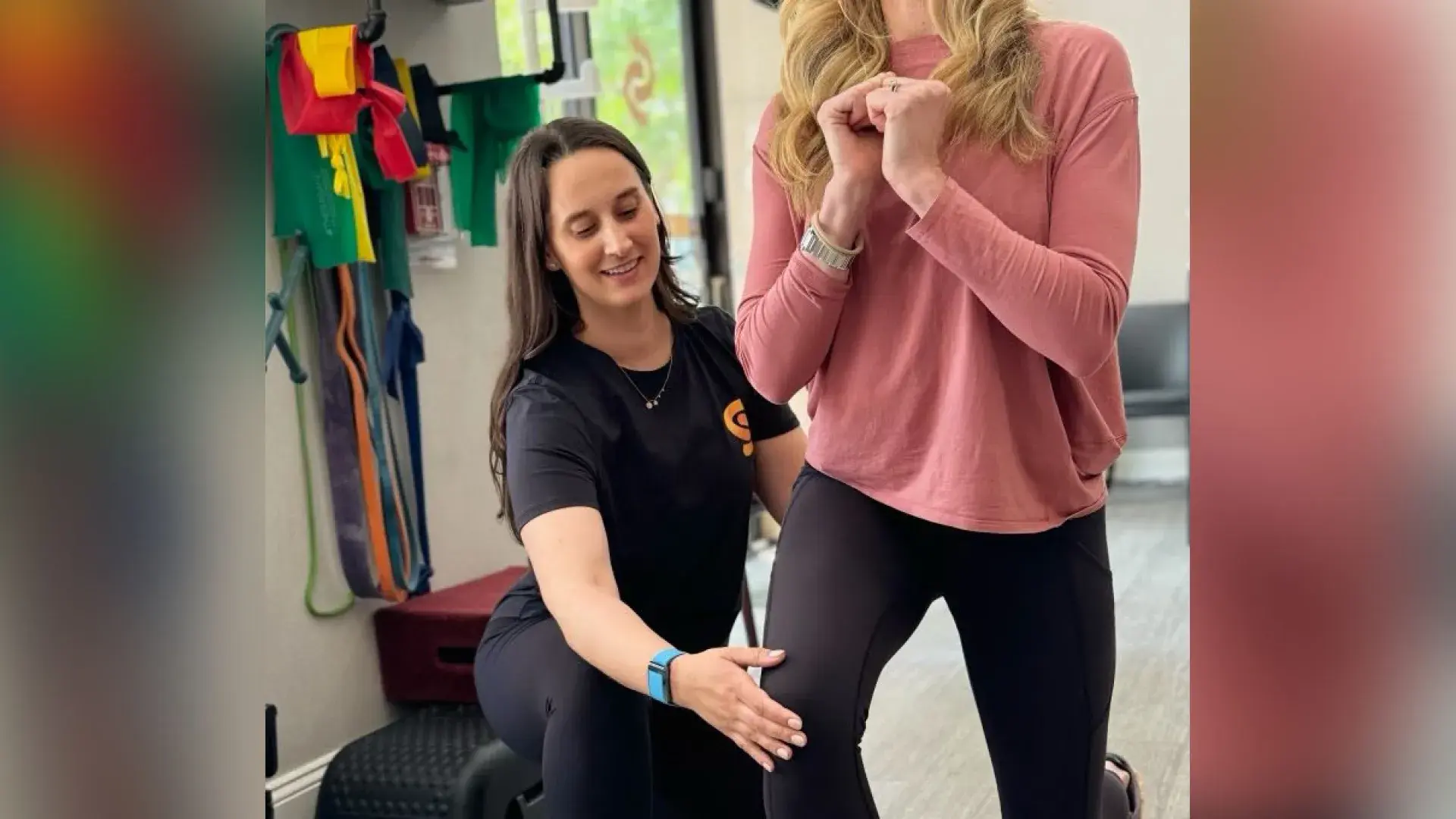 A woman kneels next to a person who is performing a lunge in a rehabilitation setting