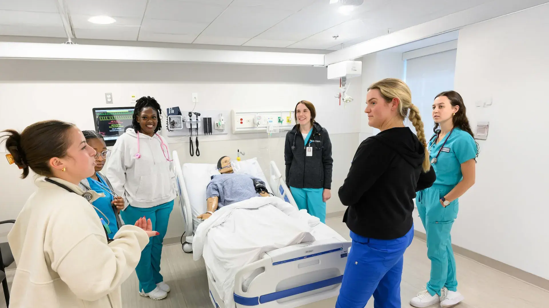 women in scrubs around a manikin in a hospital bed