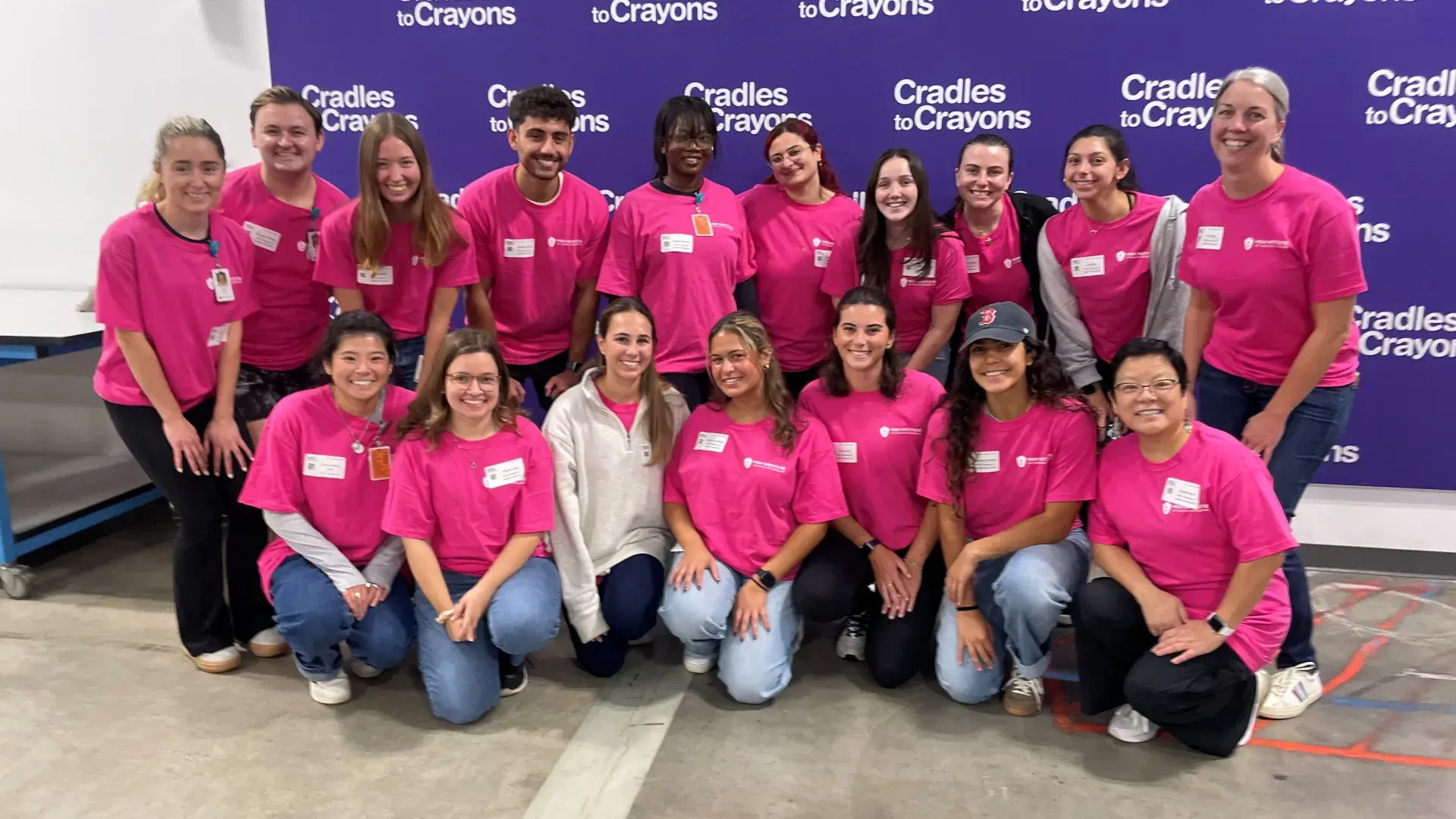 A group of people pose in front of a backdrop that says Cradles to Crayons