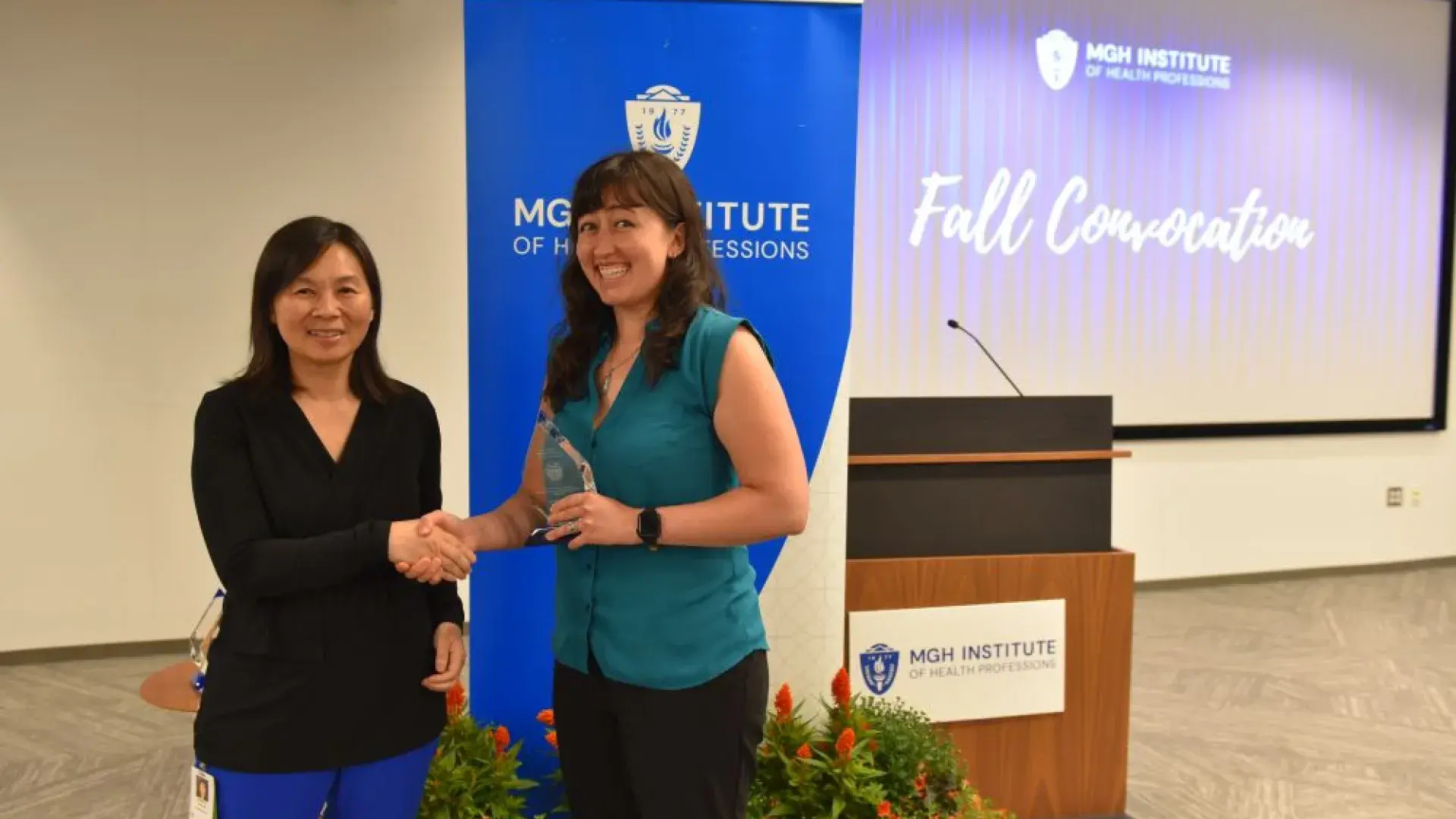 two women shaking hands with award