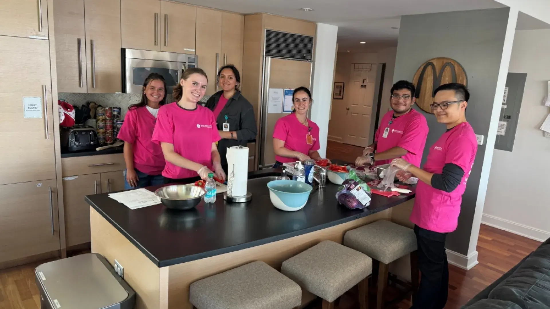 People wearing pink shirts stand around a kitchen island 
