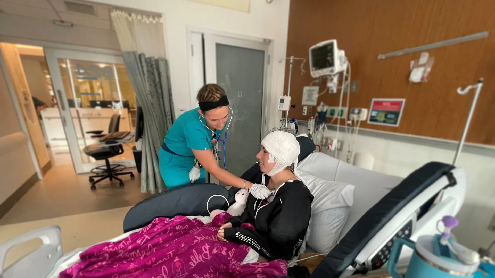 woman in scrubs holds a stethoscope to a woman's chest in a hospital bed