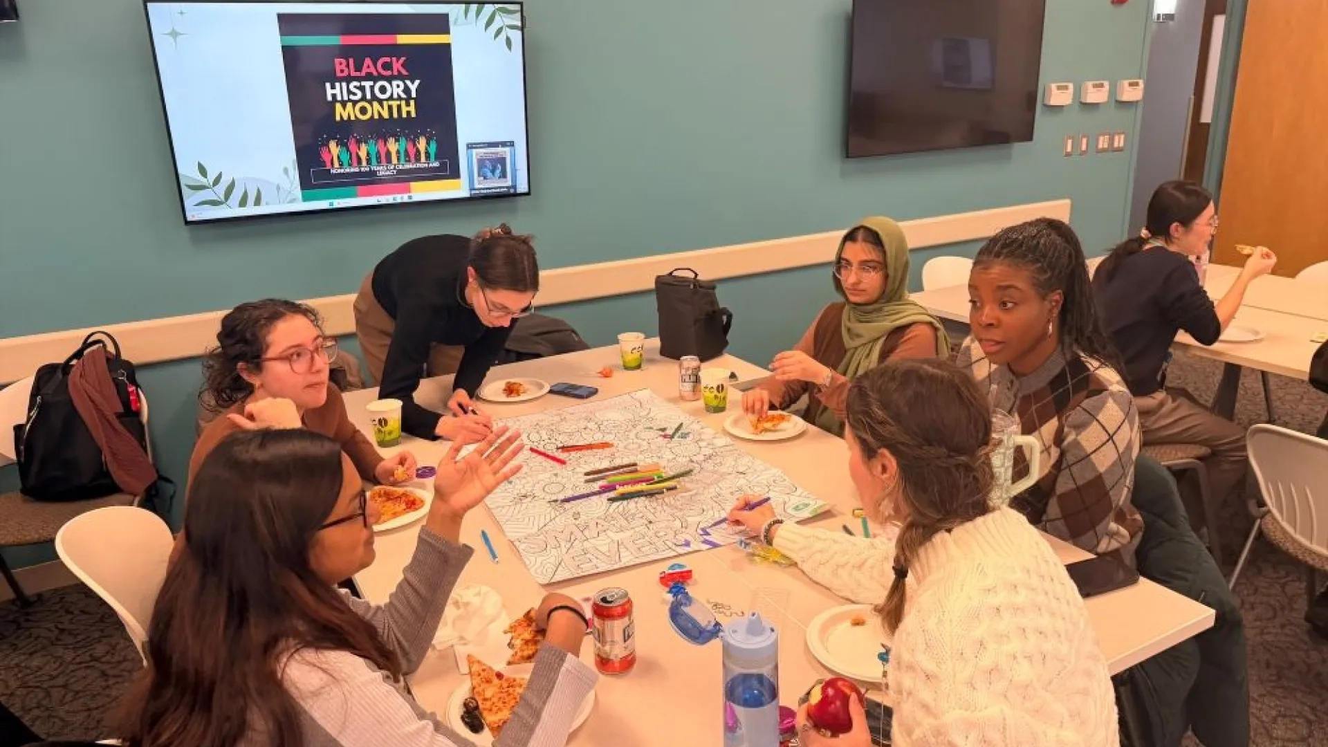 Six women sitting around a table eating and talking while two color a large sheet of paper