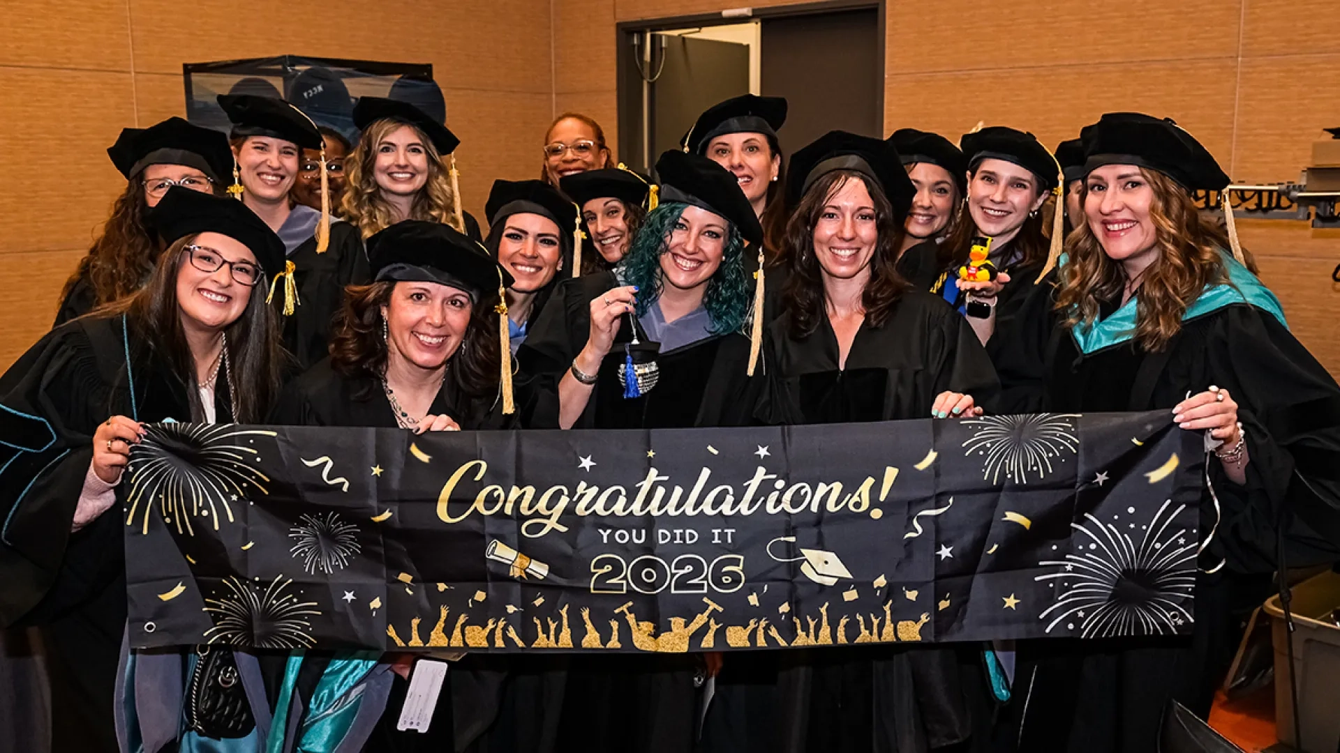 A group of people in graduation robes and hats hold a congratulations sign