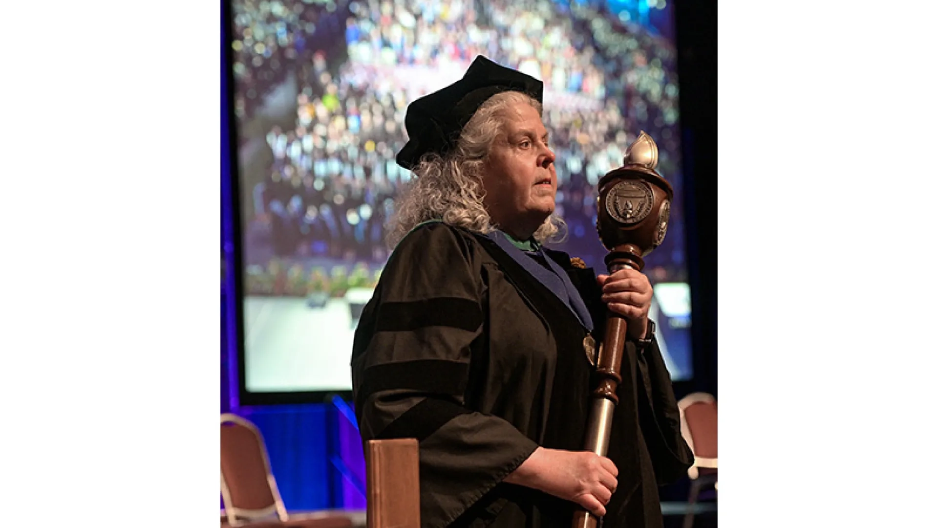 A woman holding a scepter and wearing a graduation gown at a commencement