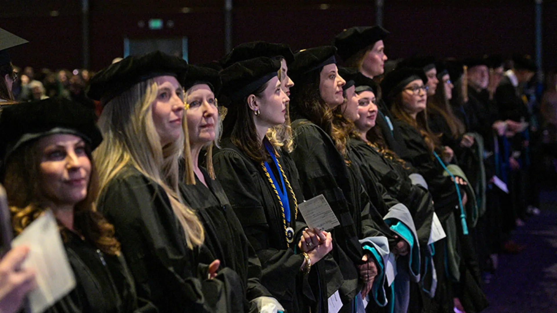 A row of people wearing graduation gowns and holding hoods at the 2026 commencement