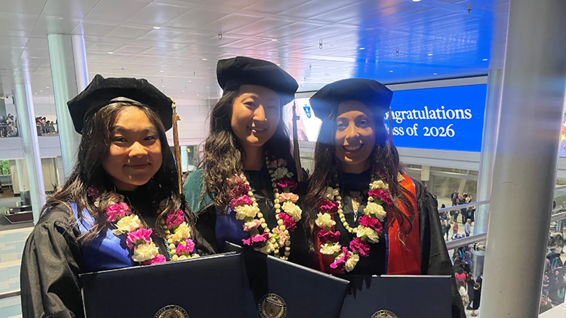 Three women wearing graduation gowns and leis