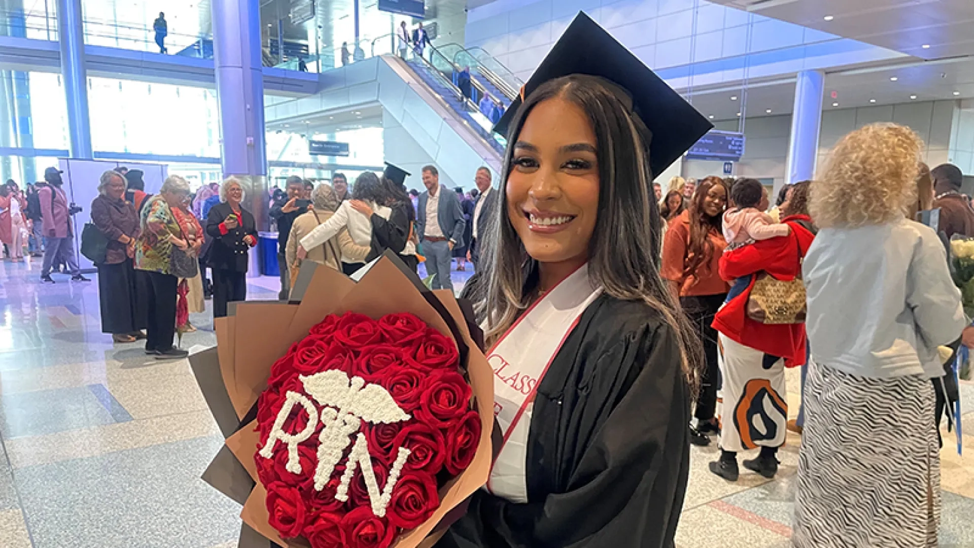 A woman wearing a graduation gown and cap holding a bouquet of flowers that spells out RN