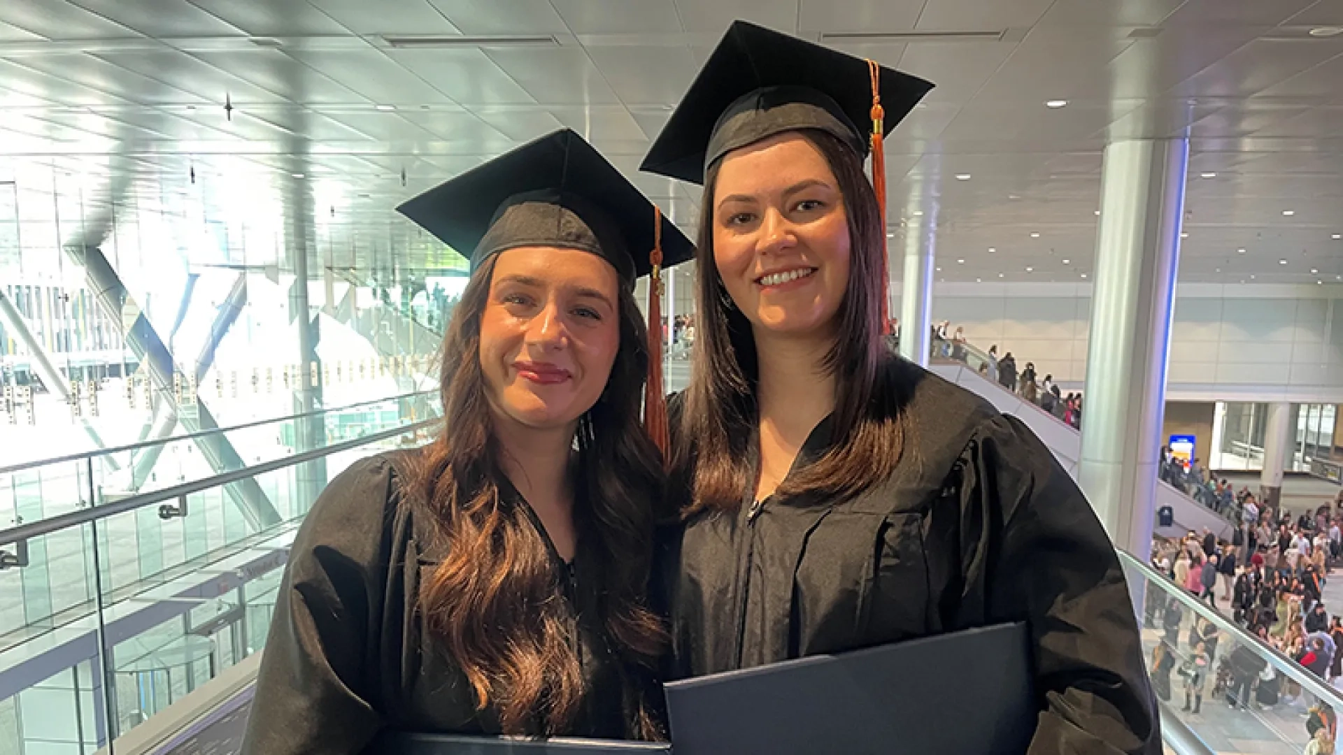 Two women wearing graduation gowns and caps while holding diplomas