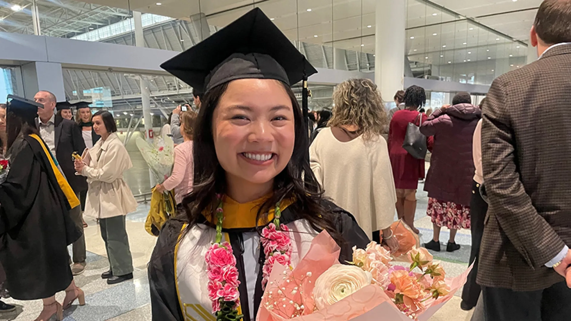 A woman wearing graduation robe while holding flowers