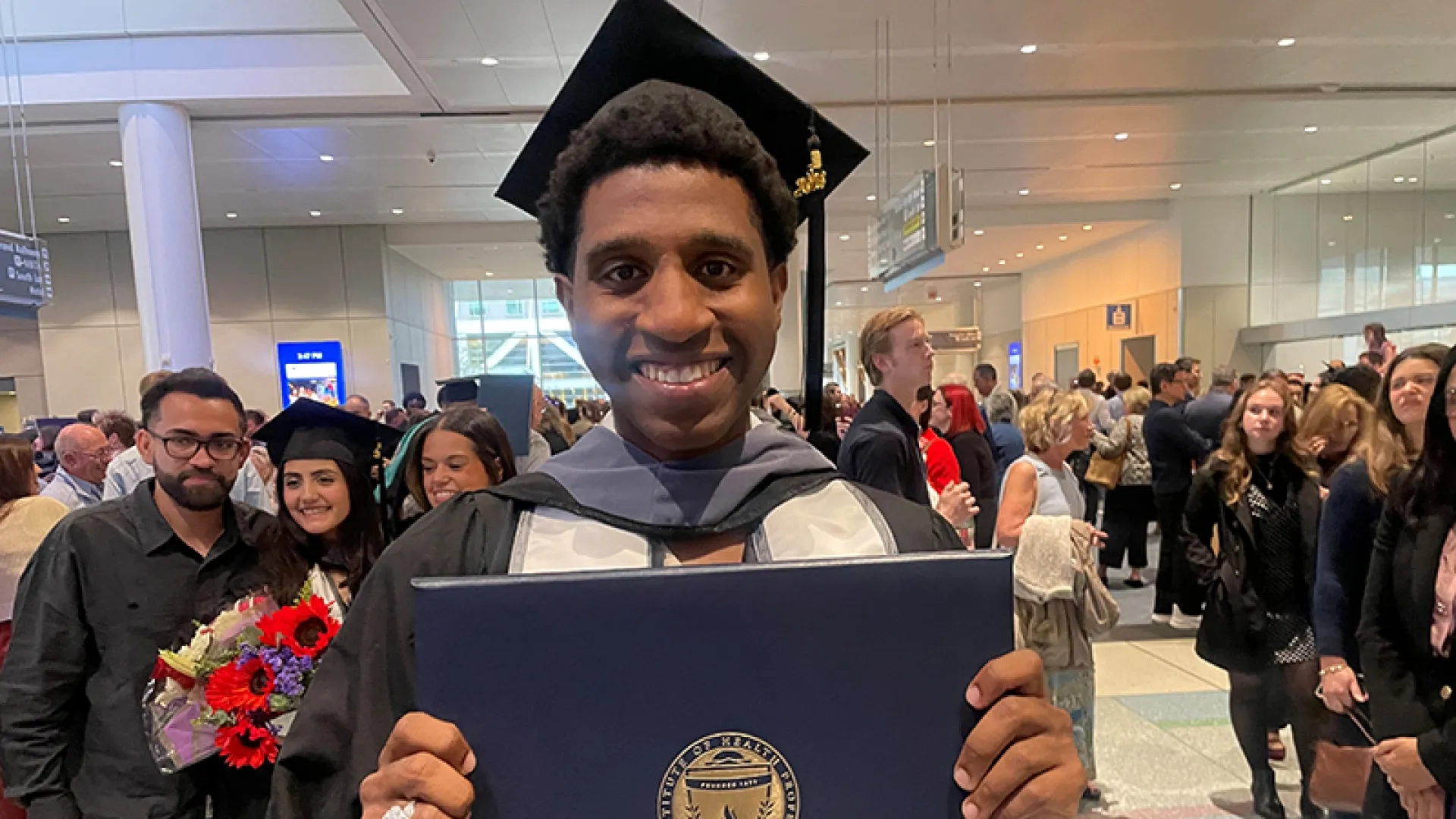 A man wearing a graduation gown and hat holding a diploma