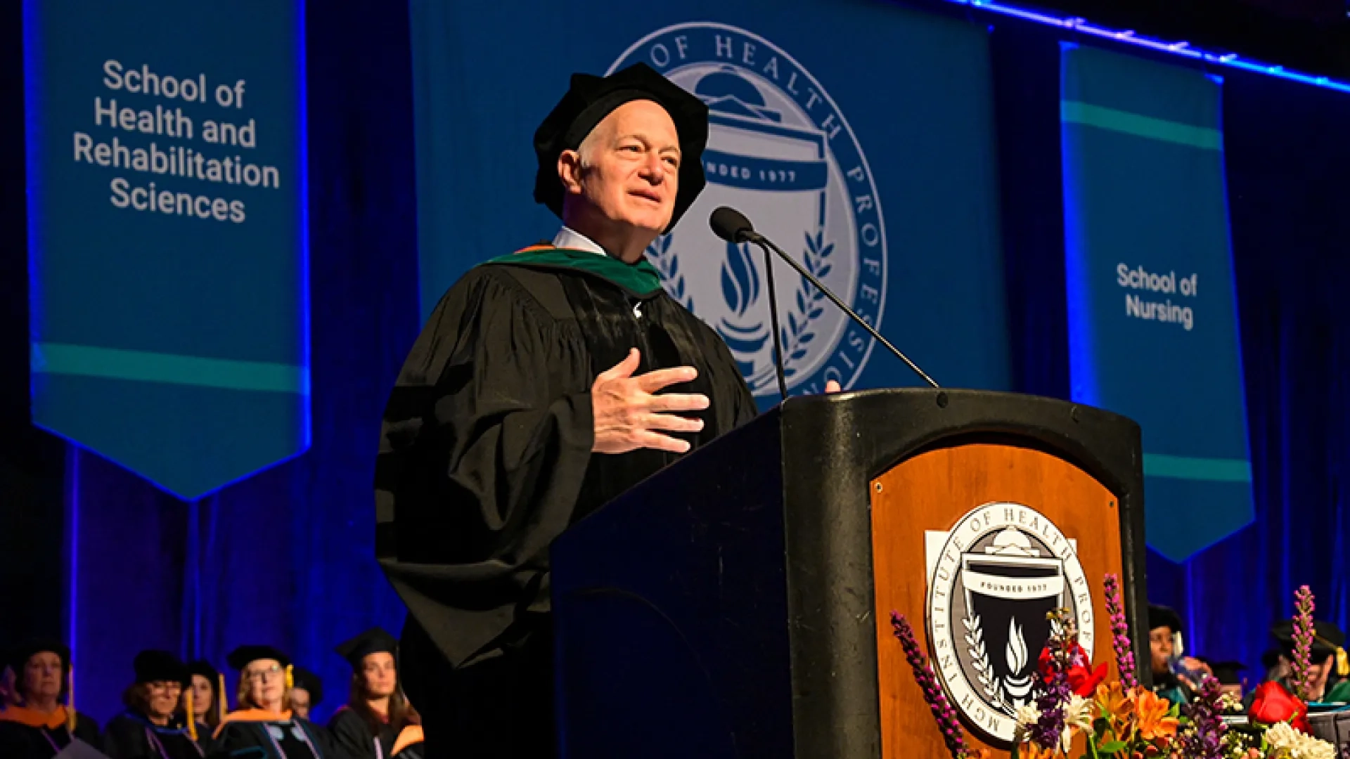 A man wearing a graduation gown and hat speaks at a podium at commencement