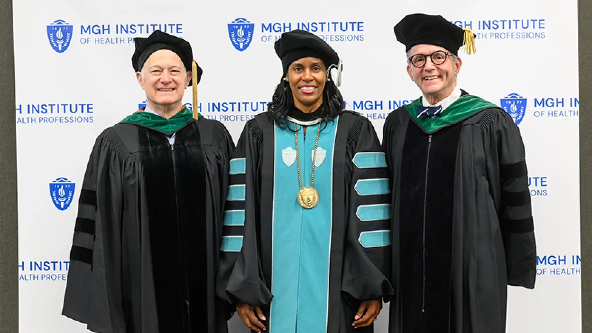 David Brown, Deborah Jones and John Herman stand in front of a backdrop with MGH Institute of Health Professions written on it. 