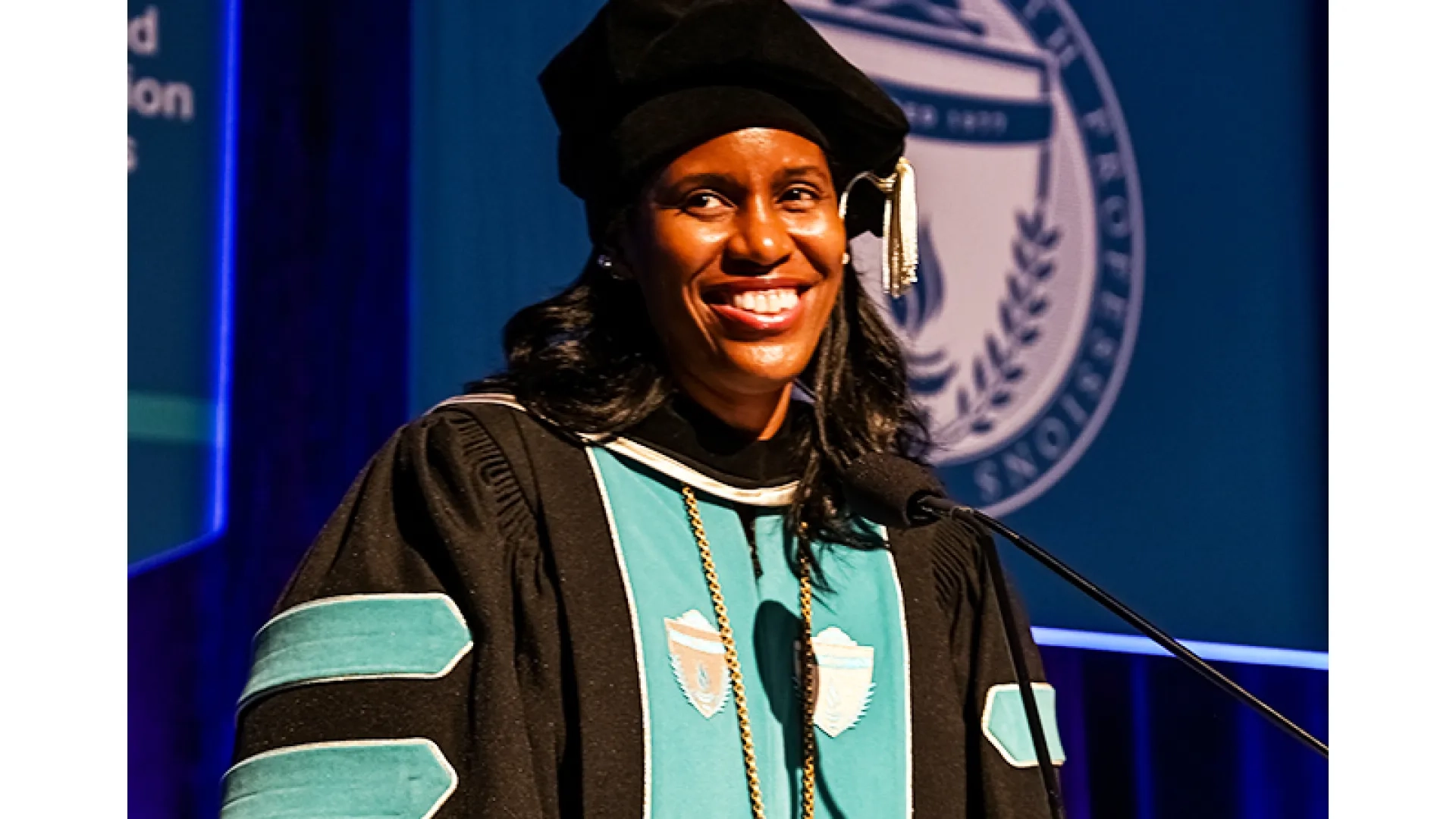 A woman stands at a podium wearing graduation robes at the 2026 commencement  