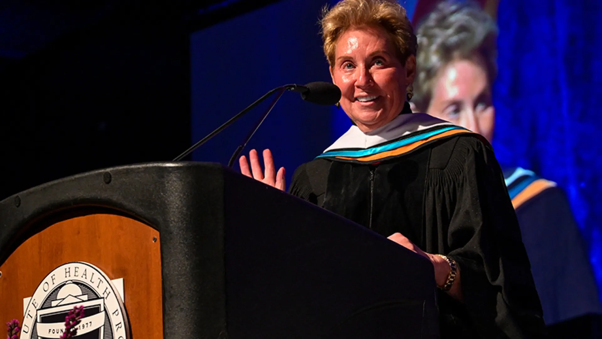 A woman wearing a graduation gown speaks at commencement