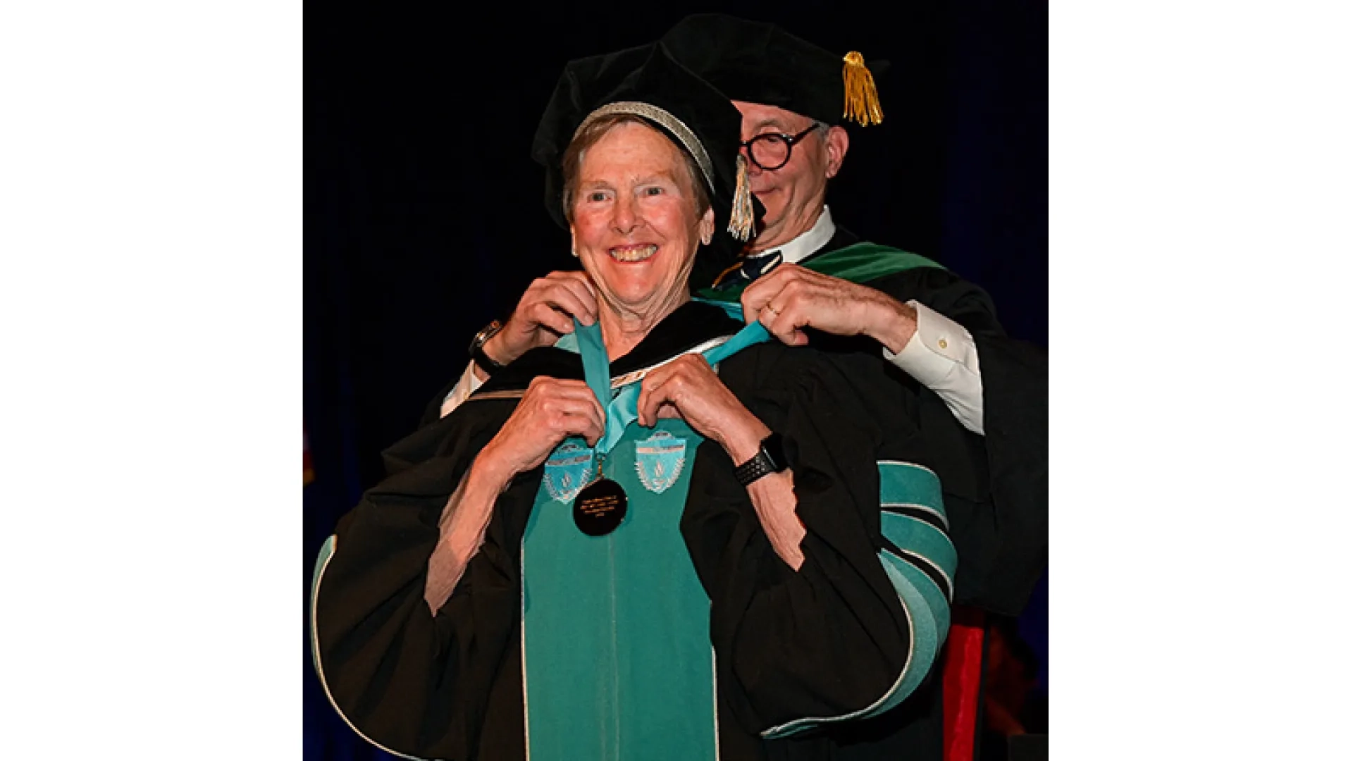 A woman has a medal being put around her neck by a man behind her at a commencement ceremony