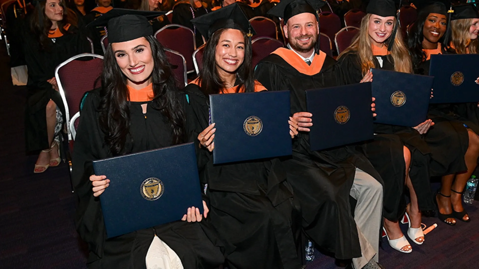 A row of people wearing graduation gowns and holding diplomas at the 2026 commencement