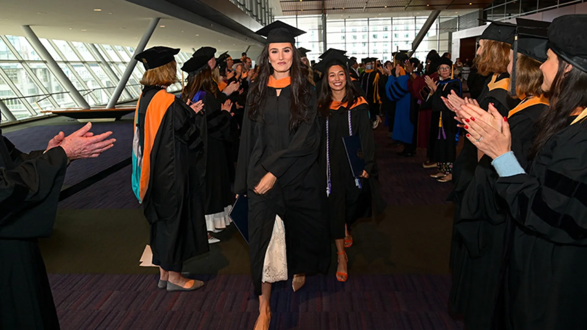 A line of graduates walks toward the camera through a tunnel made by faculty members