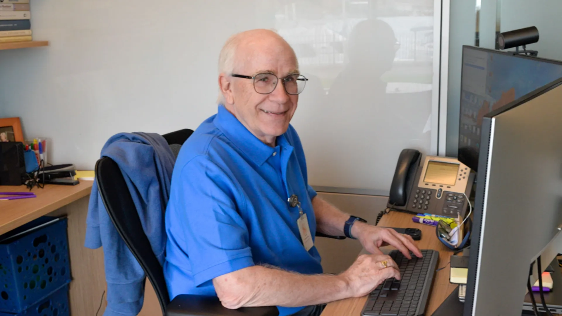 man in a blue shirt at a computer smiling 