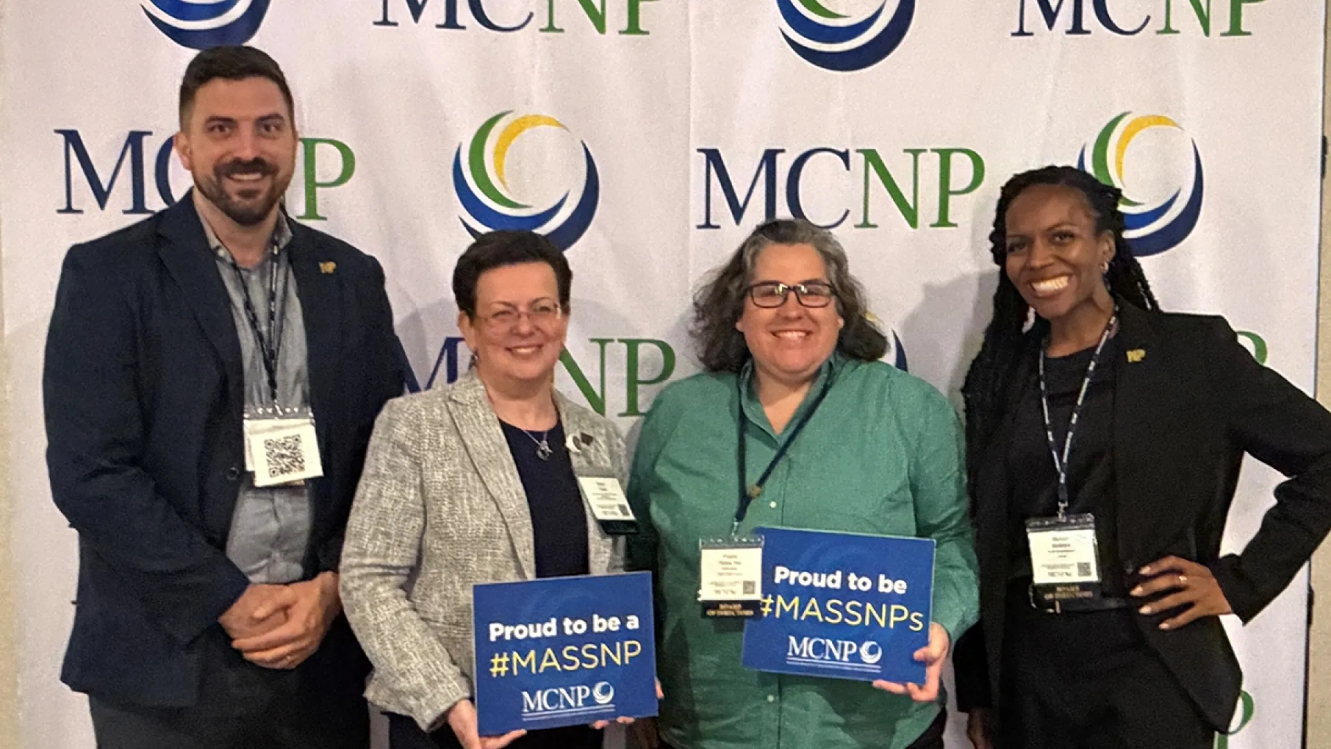 Four MGH Institute alumni pose for a photo in front of a banner for MCNP
