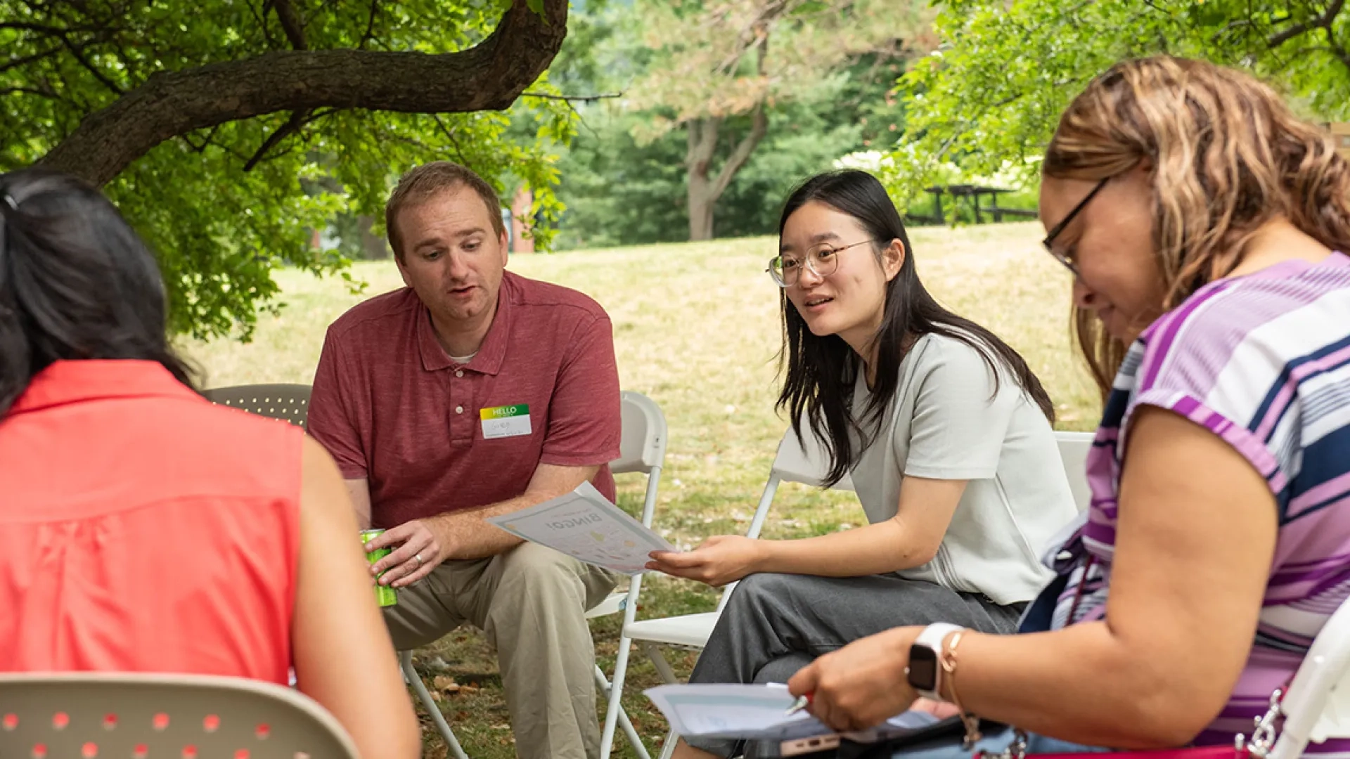 People sitting in chairs in a circle holding pieces of paper and talking to each other