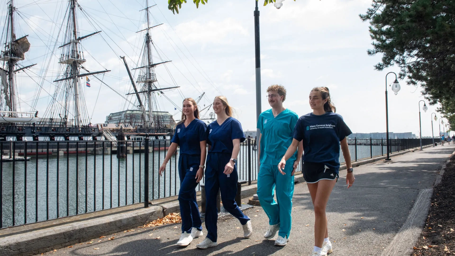 Four students wearing scrubs and T-shirts with the Mass General Brigham University of Health Professions name
