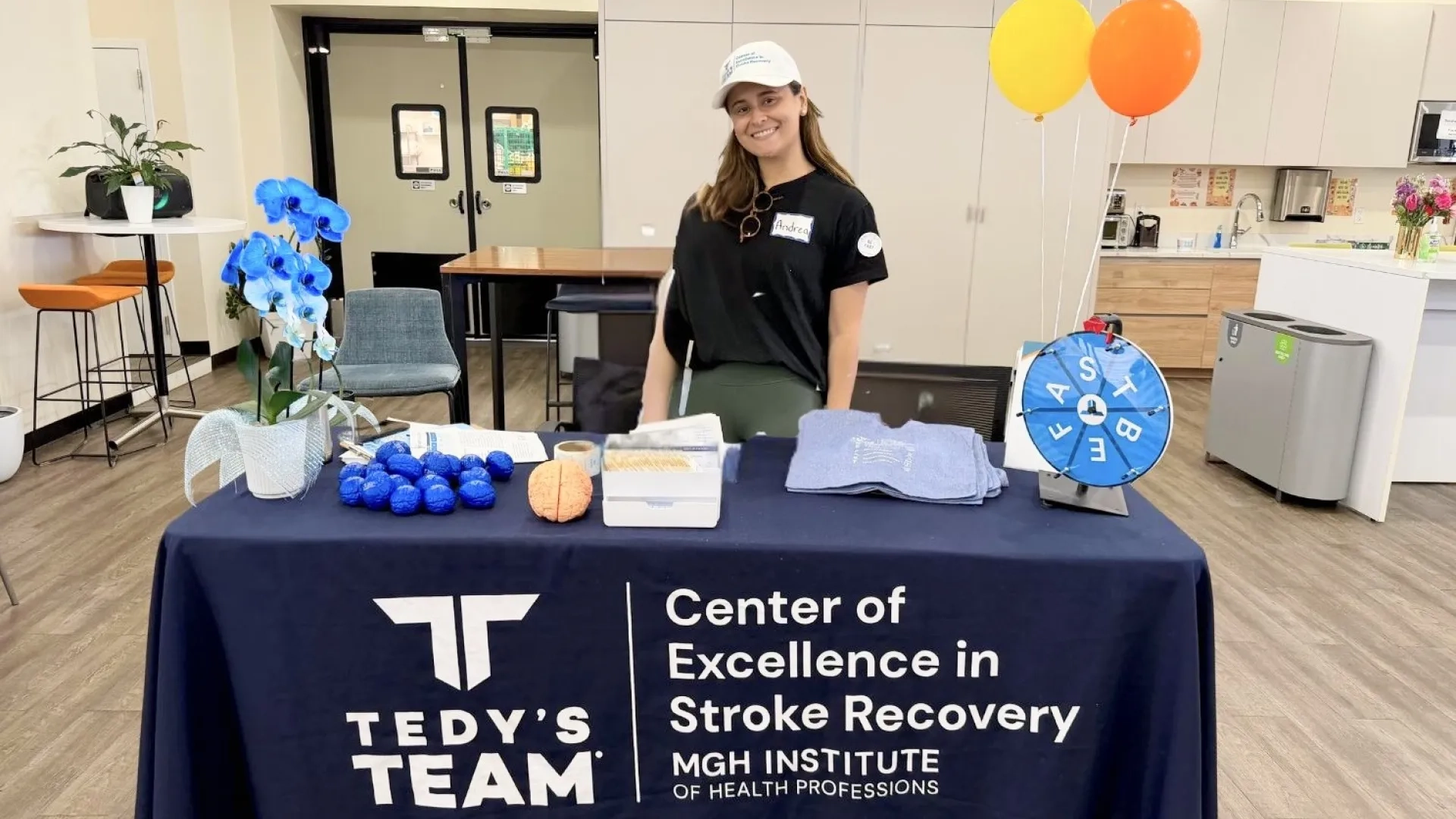 a woman in a white baseball cap smiles behind a tedy's team table at an event