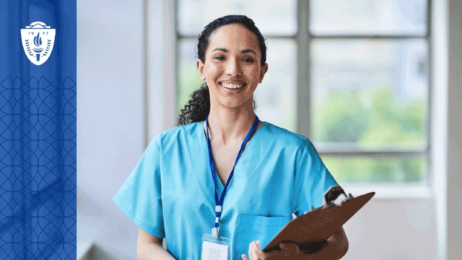 Nursing wearing blue scrubs holding a clipboard and wearing a lanyard around her neck