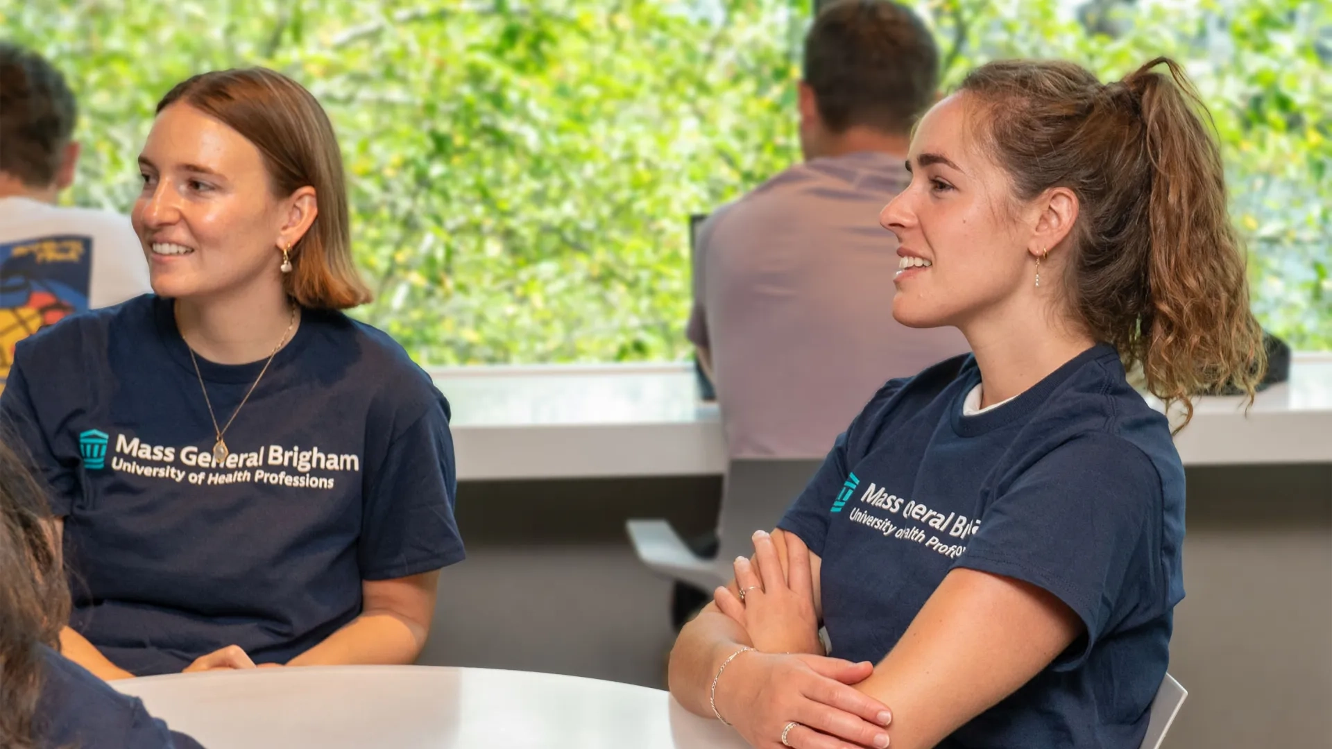 two women with Mass General Brigham University t-shirts sit at a table