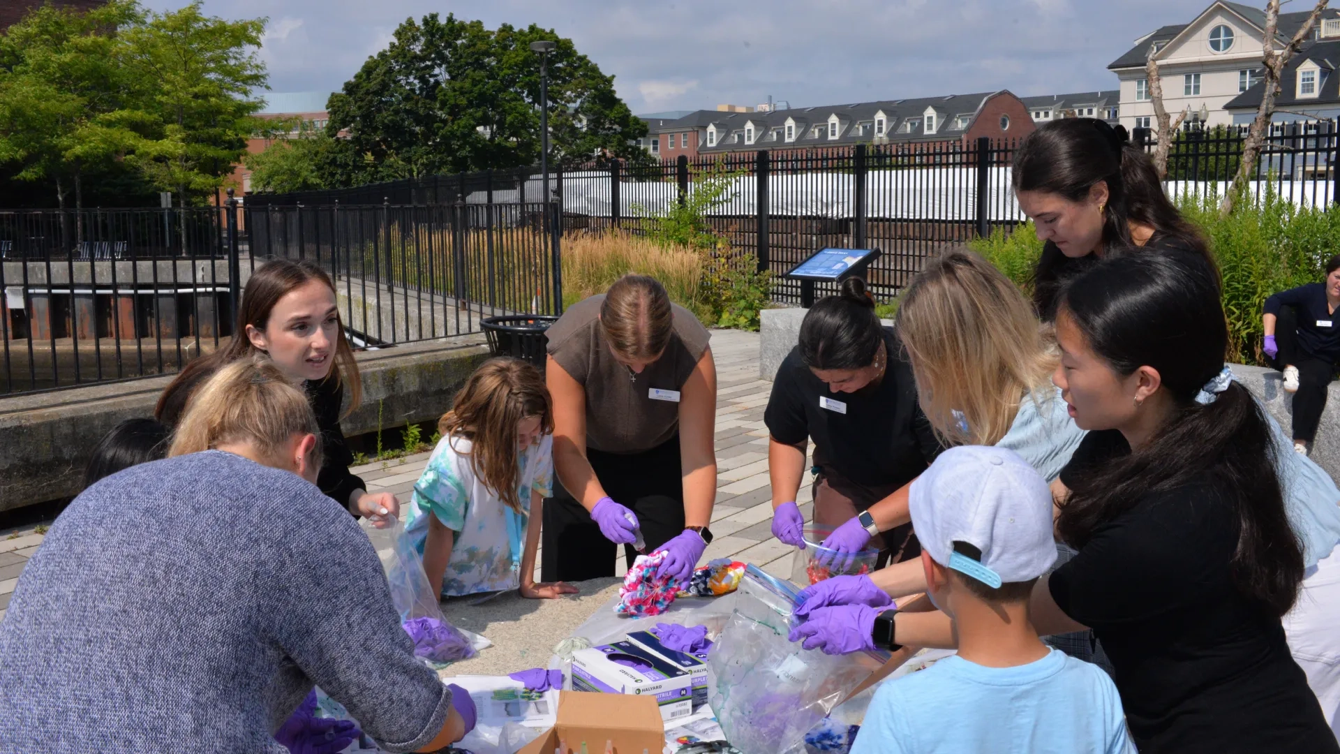 Kids and adults wear purple gloves and stand around a table dying shirts